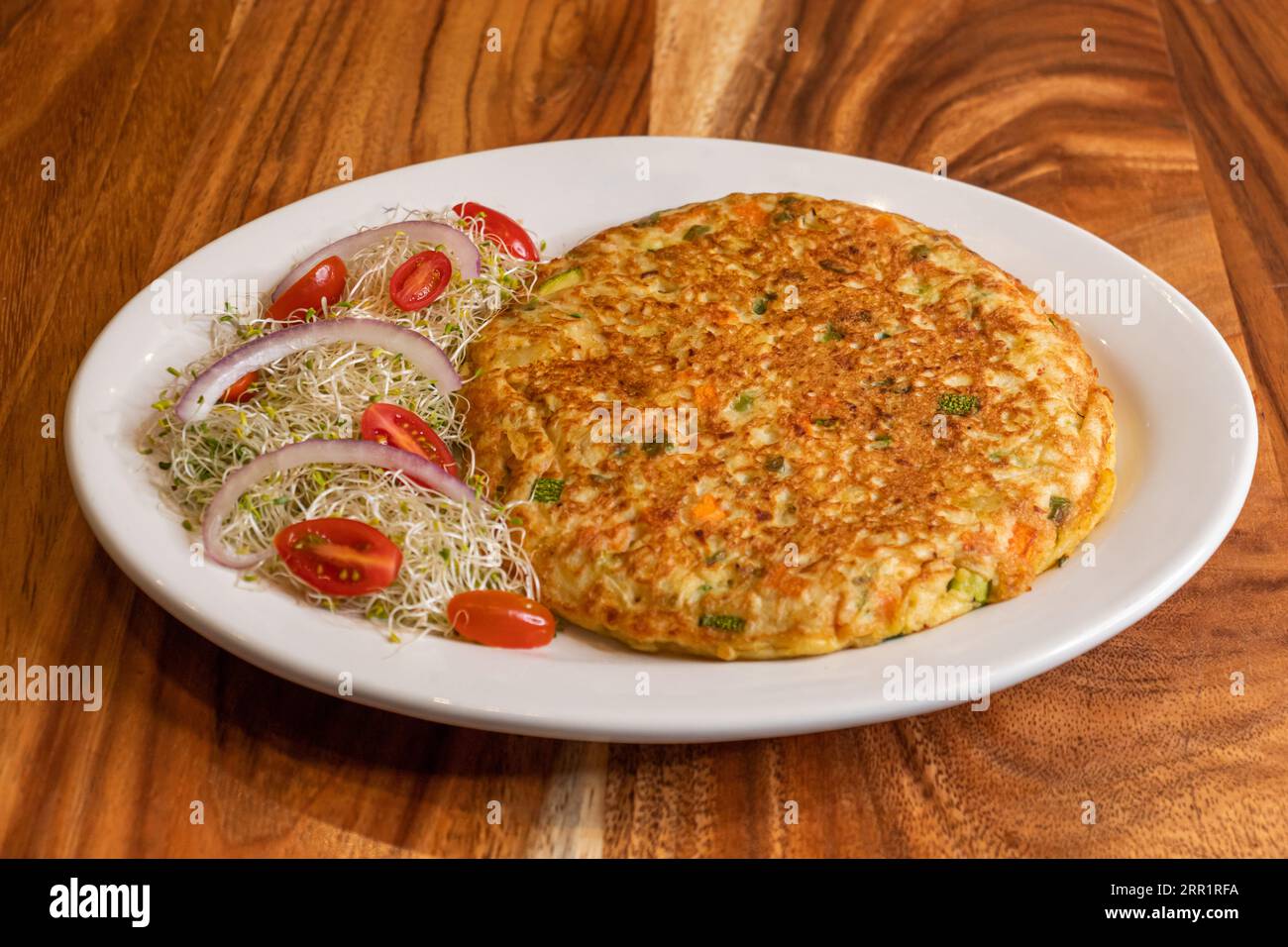 Dall'alto della deliziosa omelette preparata con cipolle tritate patate uova foglie di coriandolo, servite su piatto bianco insieme ai germogli guarniti con Foto Stock