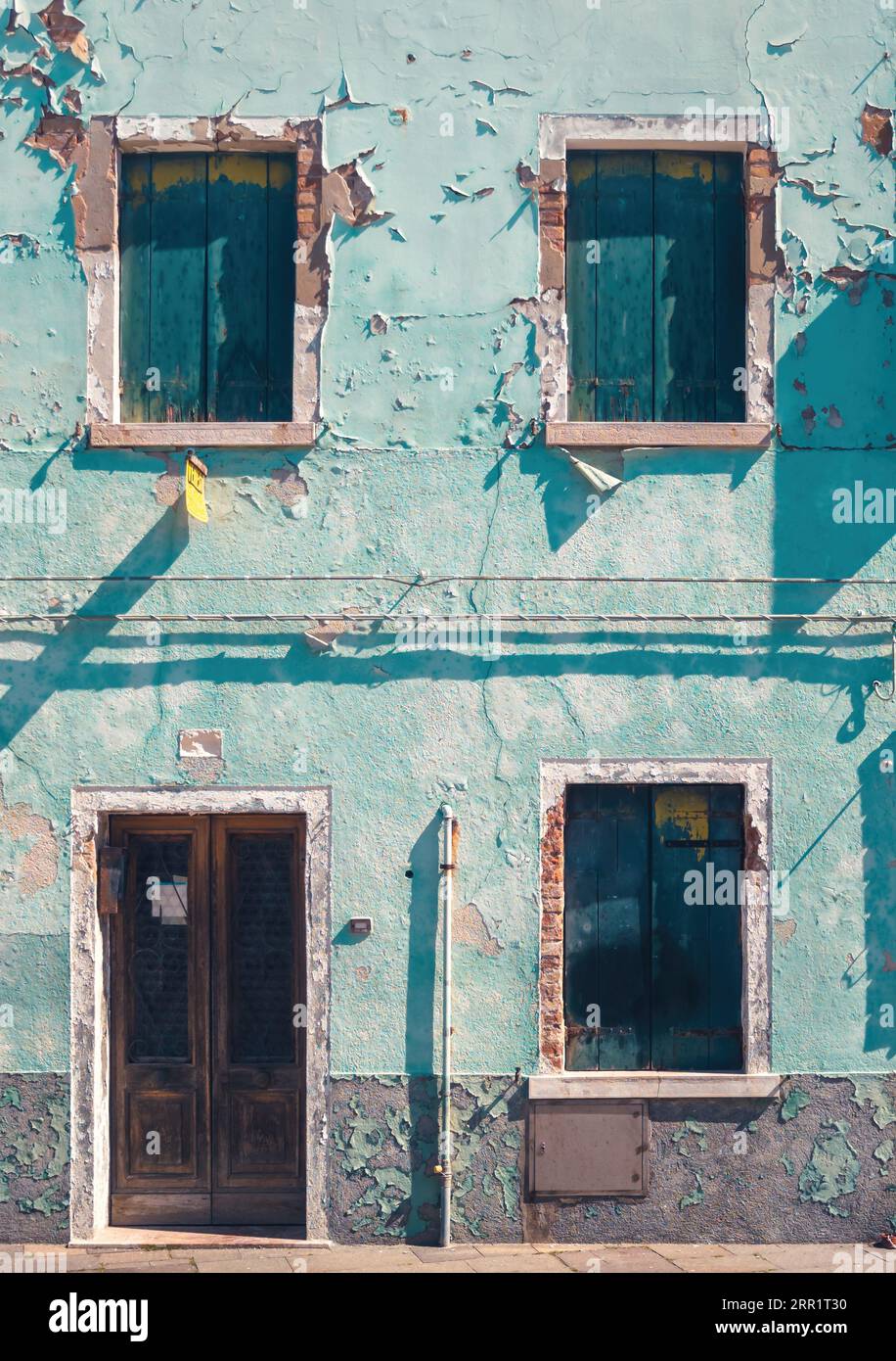 Esterno di un vecchio edificio abbandonato vuoto con porte chiuse a chiave di porte e cemento shabby che sbuccia muro blu con condutture alla luce del sole a Venezia Foto Stock