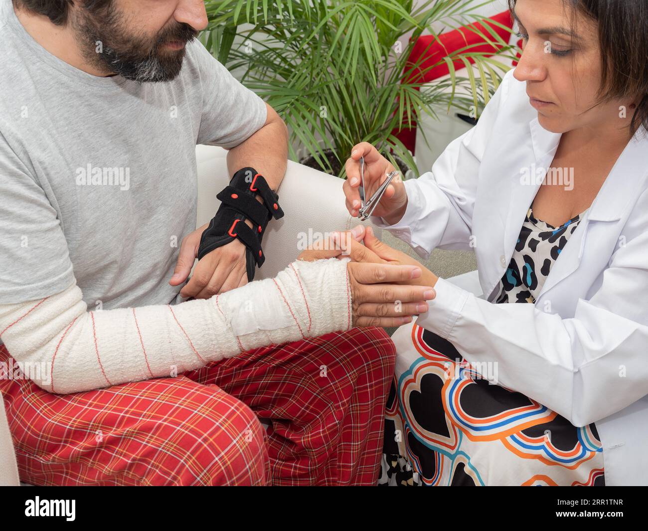 Dall'alto di infermiera femminile taglio unghie con tagliatubi per tagliare anonimi pazienti maschi con lesioni alle braccia in clinica medica Foto Stock