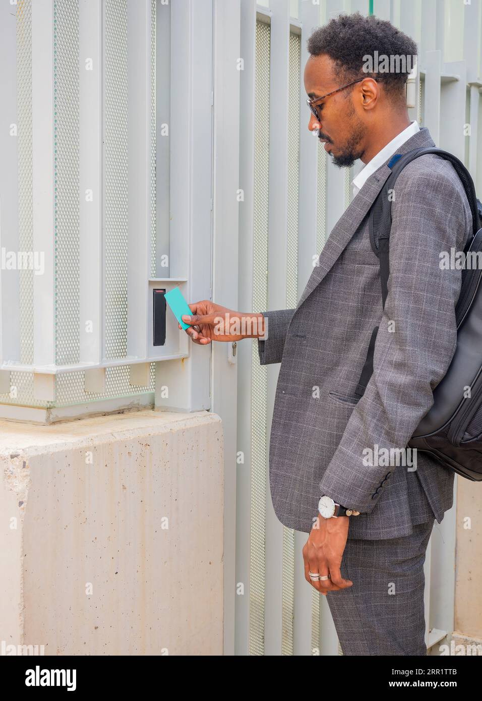 Vista laterale di un imprenditore afroamericano di sesso maschile in tuta formale che utilizza la carta d'identità di accesso di sicurezza per aprire la porta Foto Stock