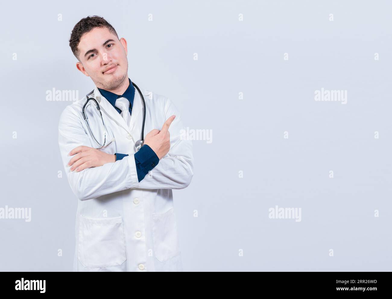 Sorridente medico latino che punta il dito in uno spazio isolato. Giovane medico che si presenta in uno spazio vuoto. Un medico che indica uno spazio bianco isolato Foto Stock