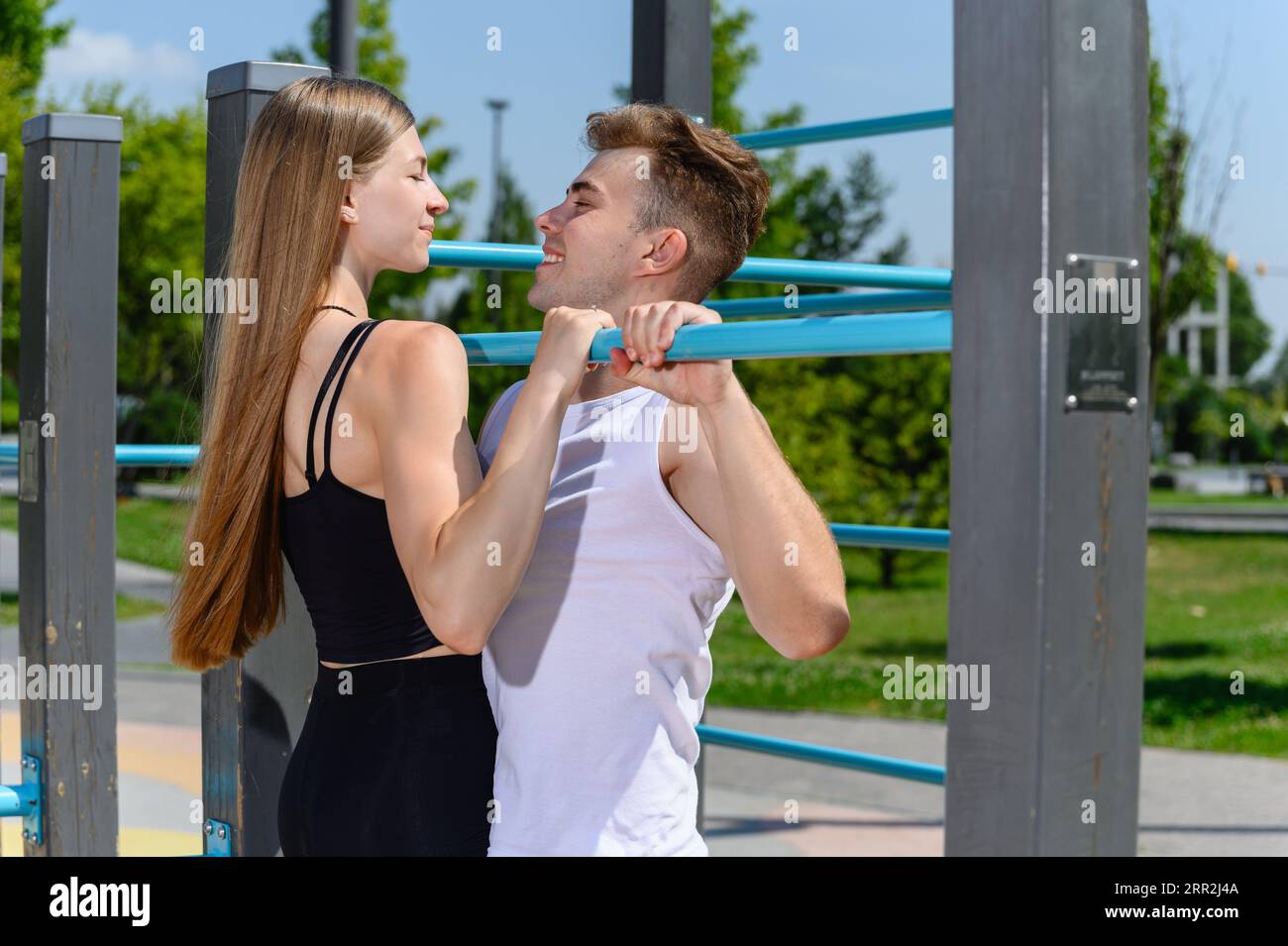 Una giovane donna attraente si tira sul bar orizzontale con un allenatore in un campo sportivo di strada per un allenamento. Foto Stock