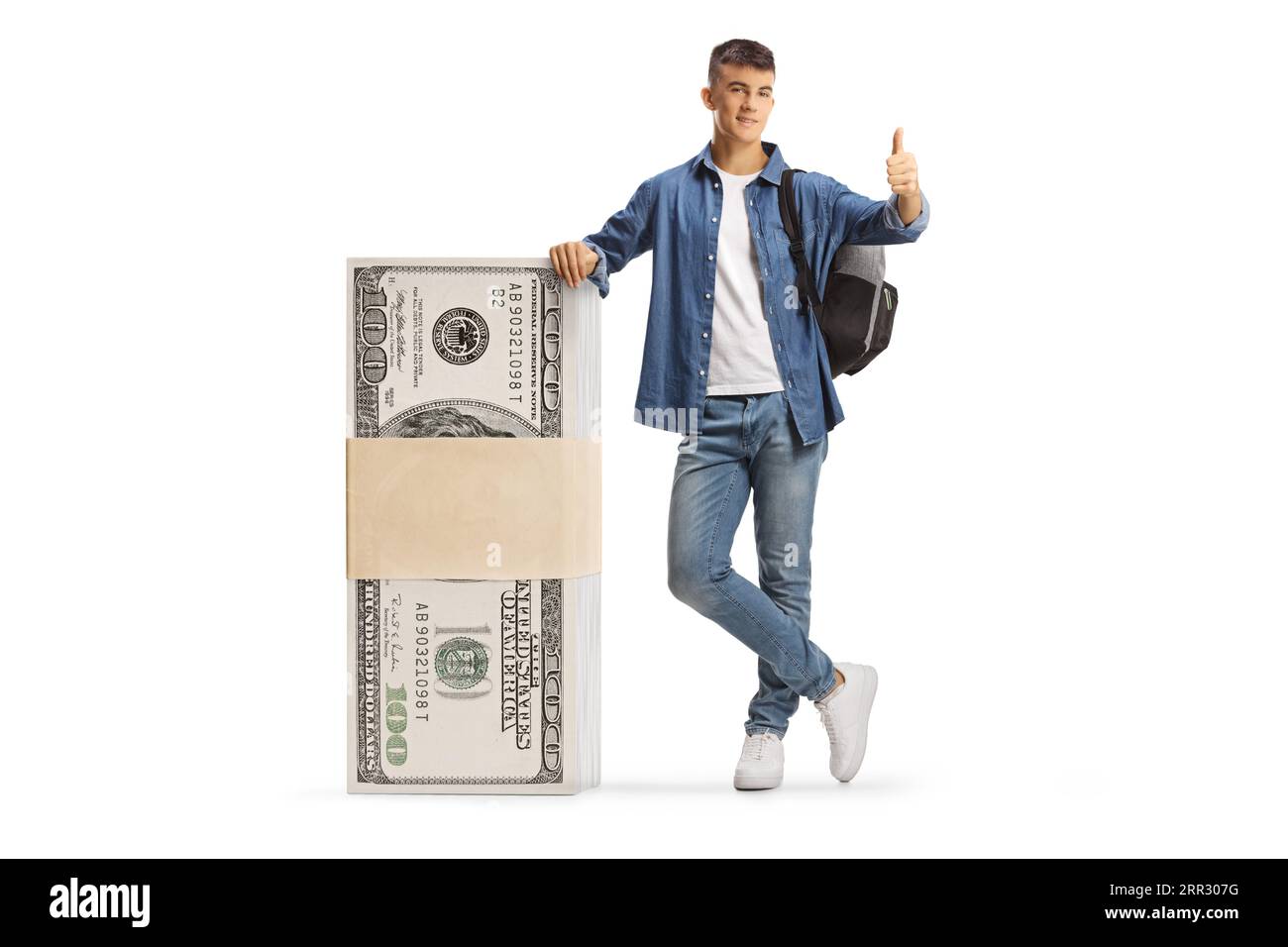 Studente maschio appoggiato su una pila di banconote da dollari e con pollice che si muove isolato su sfondo bianco Foto Stock