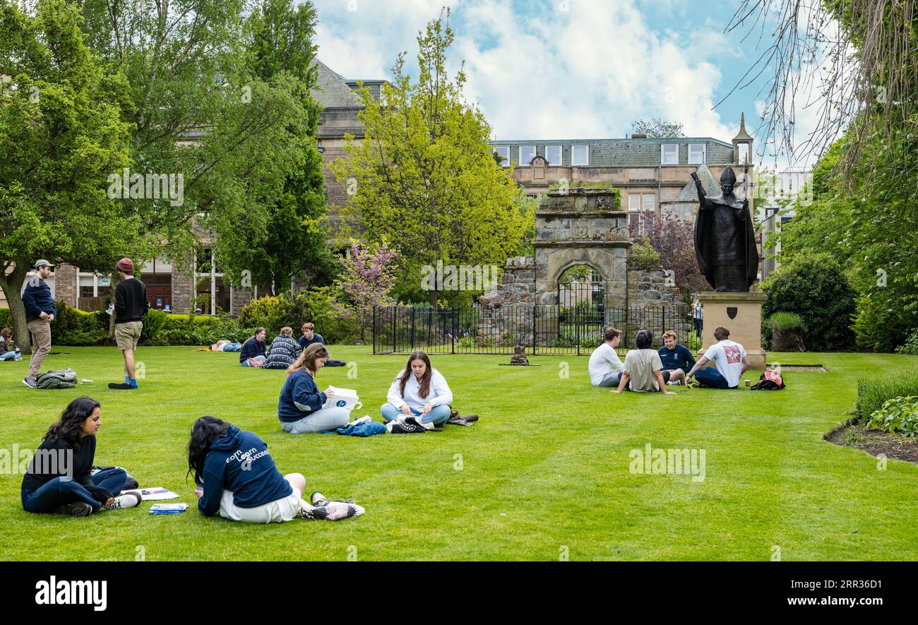Studenti seduti e rilassati sul prato erboso del St Mary's Quadrangle, St Andrews University, Fife, Scozia, Regno Unito Foto Stock