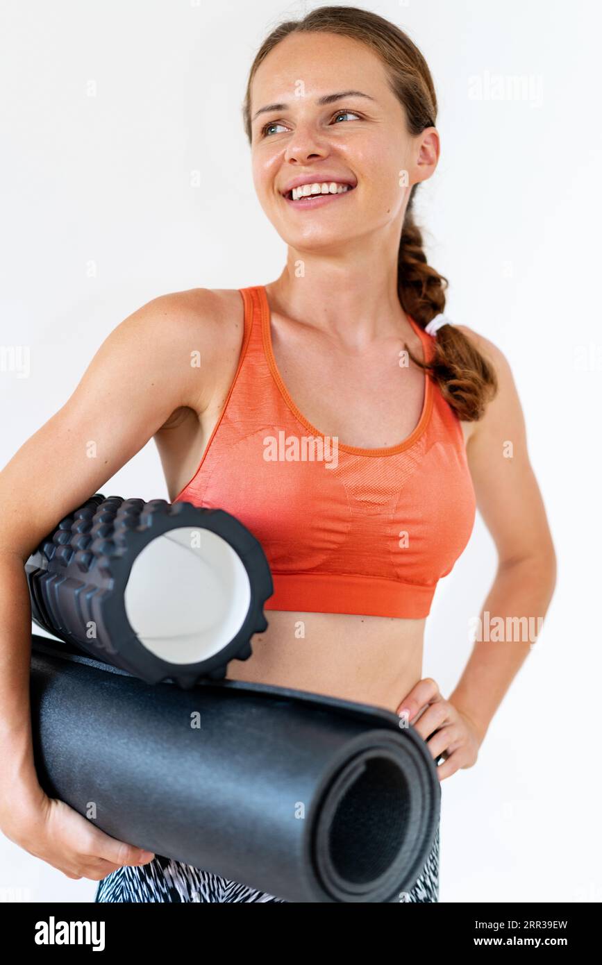 Ritratto di un'atleta istruttrice di fitness che tiene in mano il rullo di schiuma e il tappetino yoga davanti a uno sfondo bianco. Foto Stock