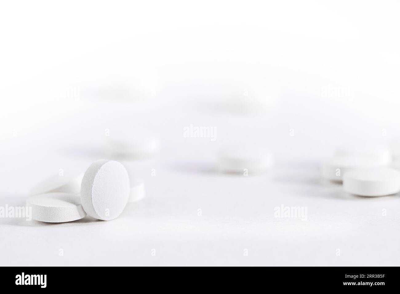Le pillole bianche sfuse si trovano su un tavolo bianco, vista frontale vuoto per lo spazio di copia del progetto. Foto Stock
