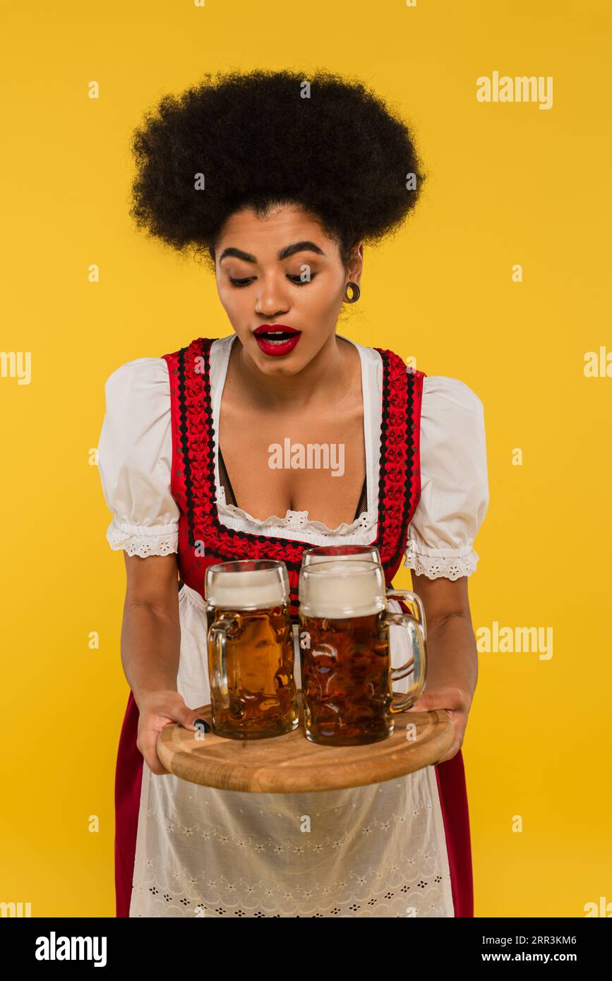 cameriera afroamericana bavarese in costume oktoberfest con tazze da birra su vassoio di legno giallo Foto Stock