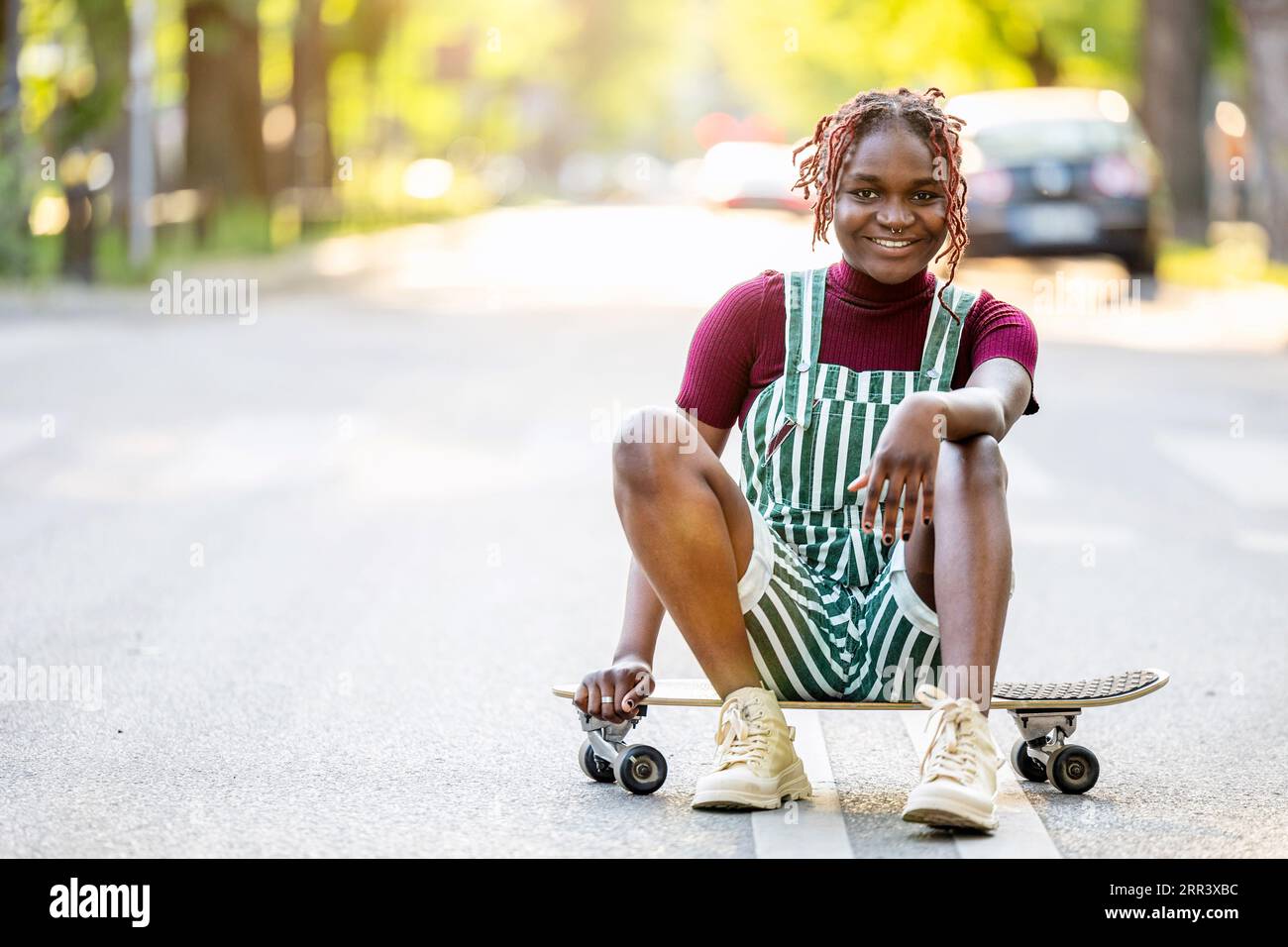 Ritratto di una persona nera non binaria con uno skateboard seduto per strada Foto Stock