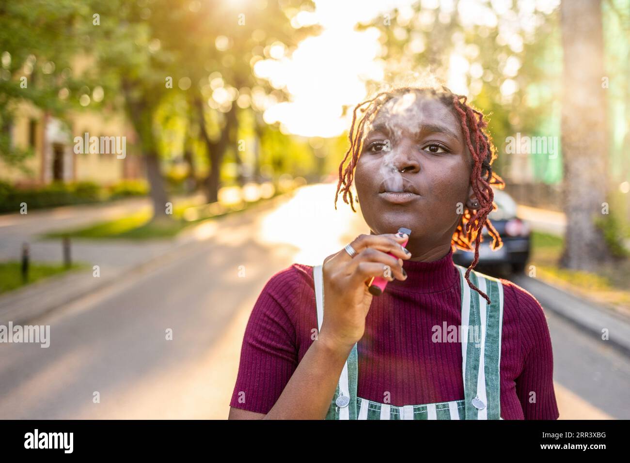 Persona nera non binaria che fuma sigaretta elettronica per strada Foto Stock