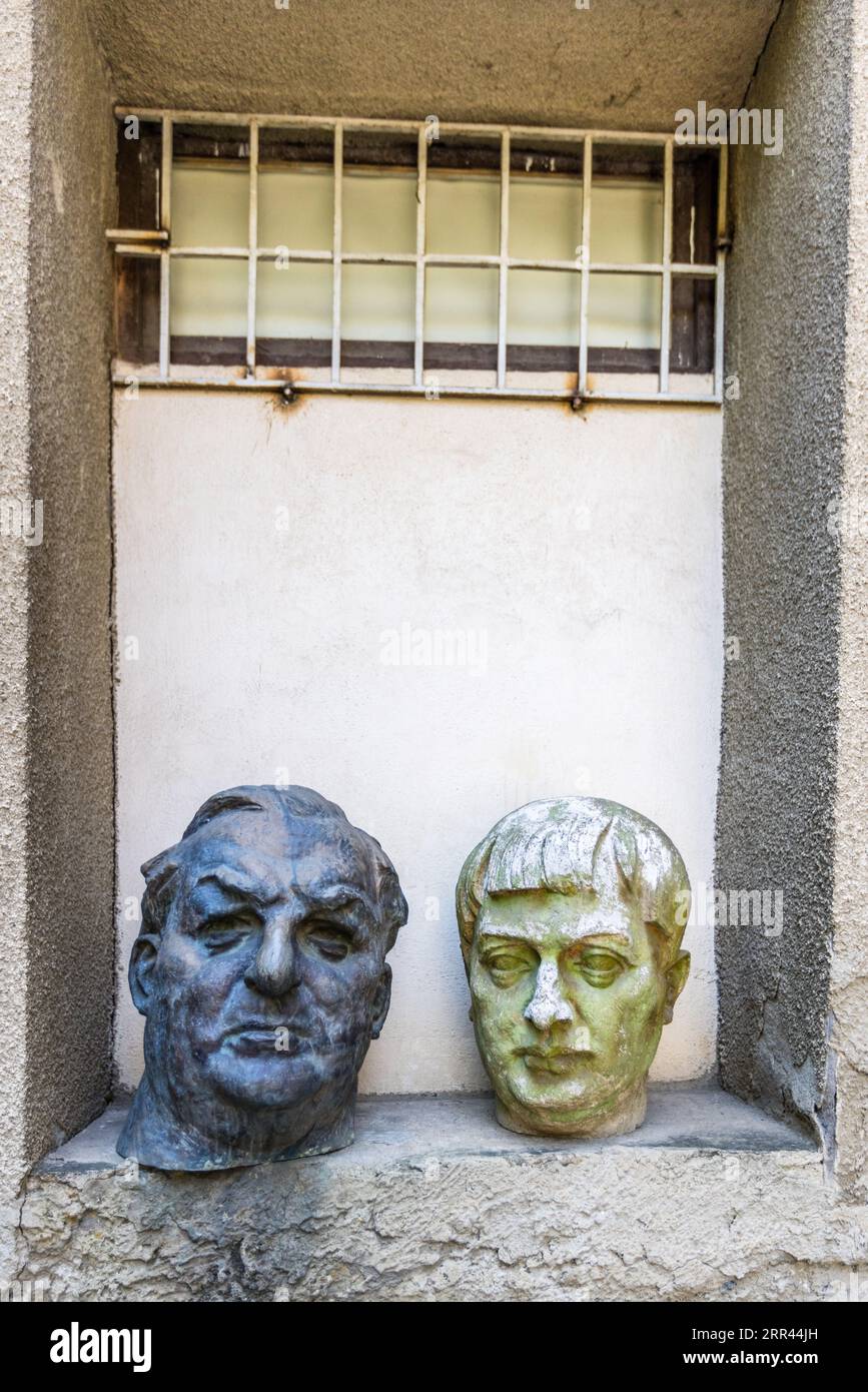Due teste si trovano in una nicchia murale sotto una finestra sbarrata su un edificio in via Gia Chanturia nel quartiere Sololaki di Tbilisi, Georgia. La testa scura a sinistra mostra un uomo anziano con sopracciglia folte e capelli pettinati all'indietro. La testa bianco-verdastra a destra mostra un giovane con una frangia. Foto Stock