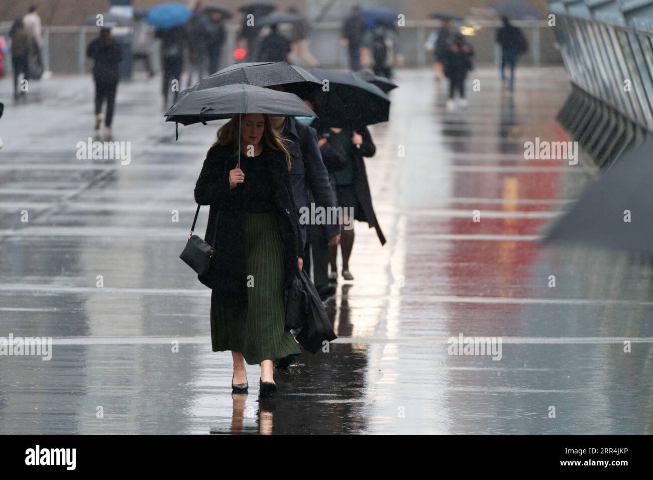 Gruppo di persone che camminano con ombrelloni in fila, in una giornata umida nella città australiana di Melbourne. Foto Stock