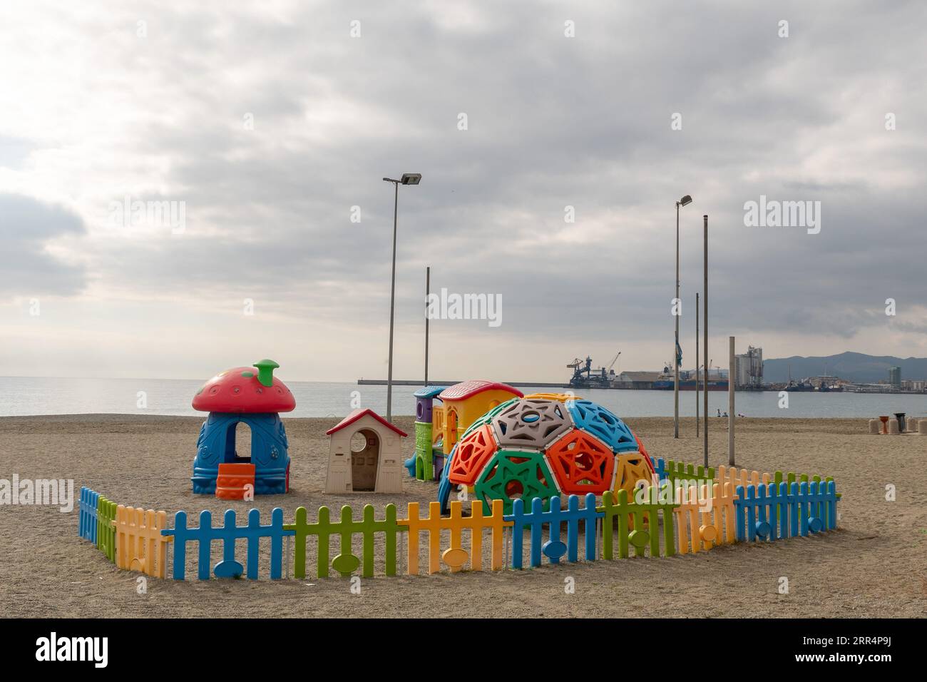 Parco giochi sulla spiaggia vuota d'inverno con il porto di Savona sullo sfondo in una giornata nuvolosa, Albissola Marina, Savona, Liguria, Italia Foto Stock