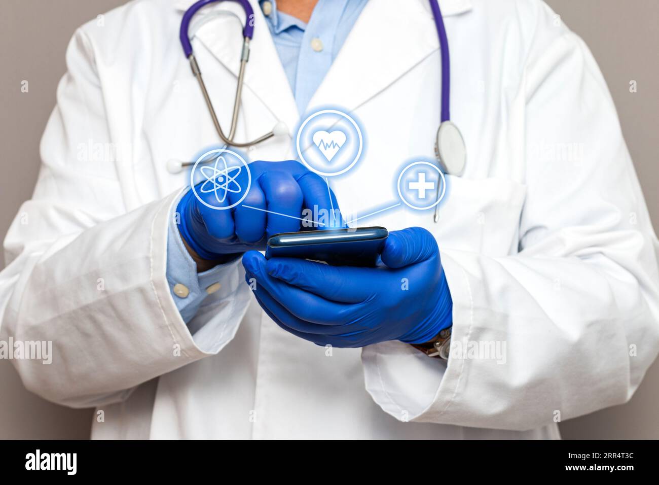 Primo piano delle mani di un medico irriconoscibile che indossa guanti blu che reggono uno smartphone mentre tocca il rasatore e tre icone sono fluttuanti. Foto Stock