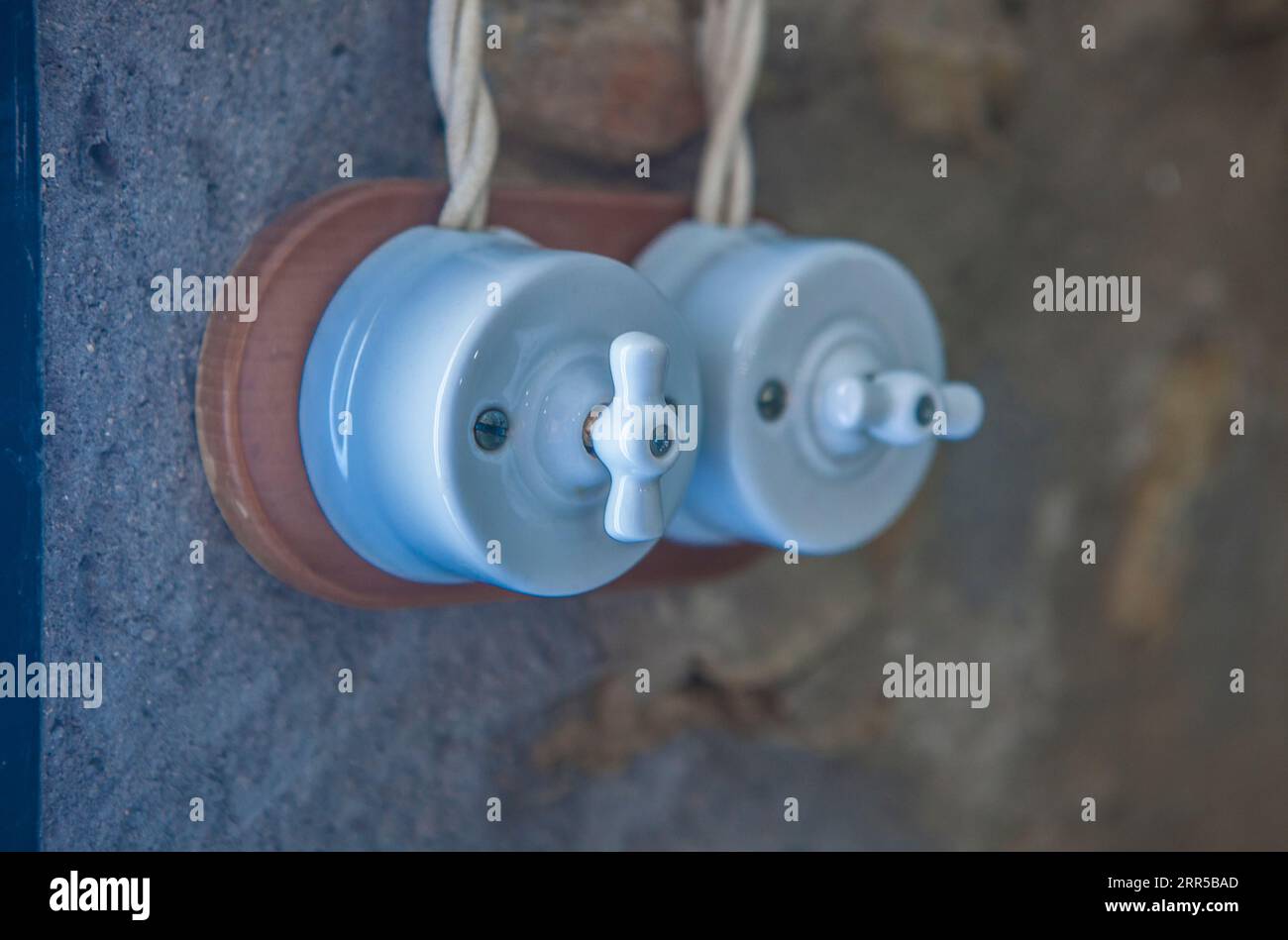 Interruttore a doppia luce in stile vintage in porcellana e legno su pareti in pietra a secco. Luce fredda Foto Stock