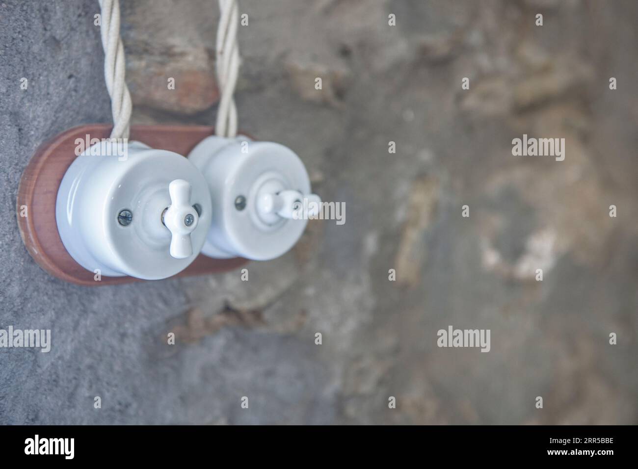 Interruttore a doppia luce in stile vintage in porcellana e legno su pareti in pietra a secco. Messa a fuoco selettiva Foto Stock