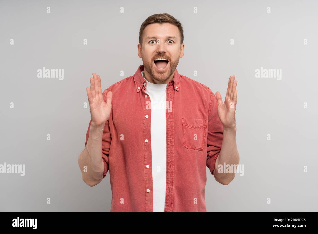 Sorpreso sorridente uomo con la bocca aperta che si estende le mani guarda la fotocamera sullo sfondo dello studio Foto Stock