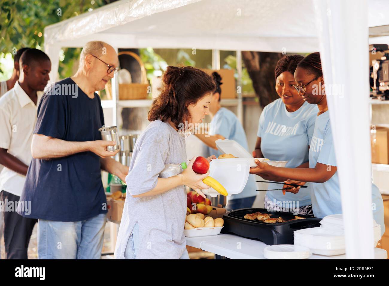 Volontari compassionevoli distribuiscono cibo gratuito e forniscono aiuti umanitari ai bisognosi. Poveri e senzatetto di diverse etnie che ricevono nutrimento dall'organizzazione no-profit. Foto Stock