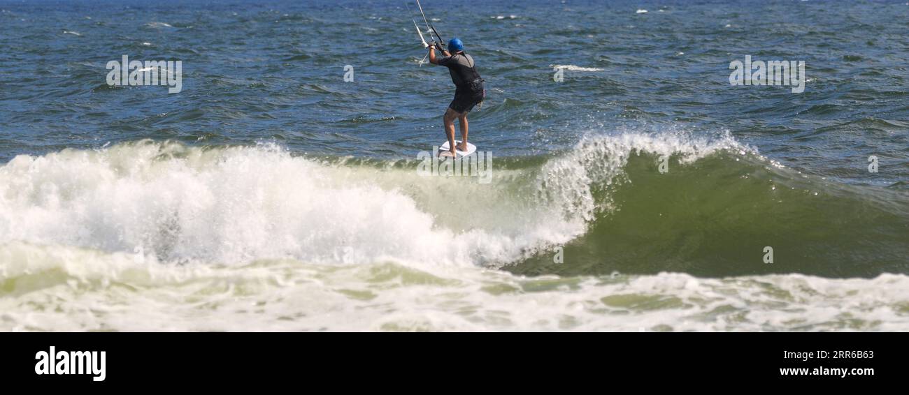 Vista posteriore di un Kitesurfer maschio che cavalca onde infranti nell'oceano al largo della costa di Long Island New York. Foto Stock