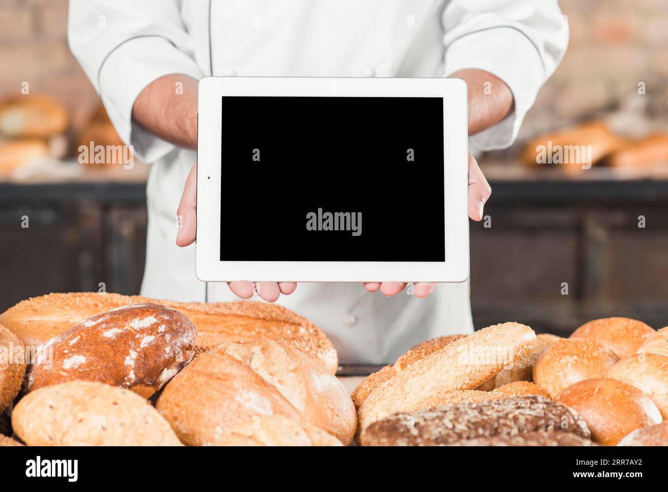 Primo piano del fornaio maschile che mostra il pane cotto in una compressa digitale vuota Foto Stock