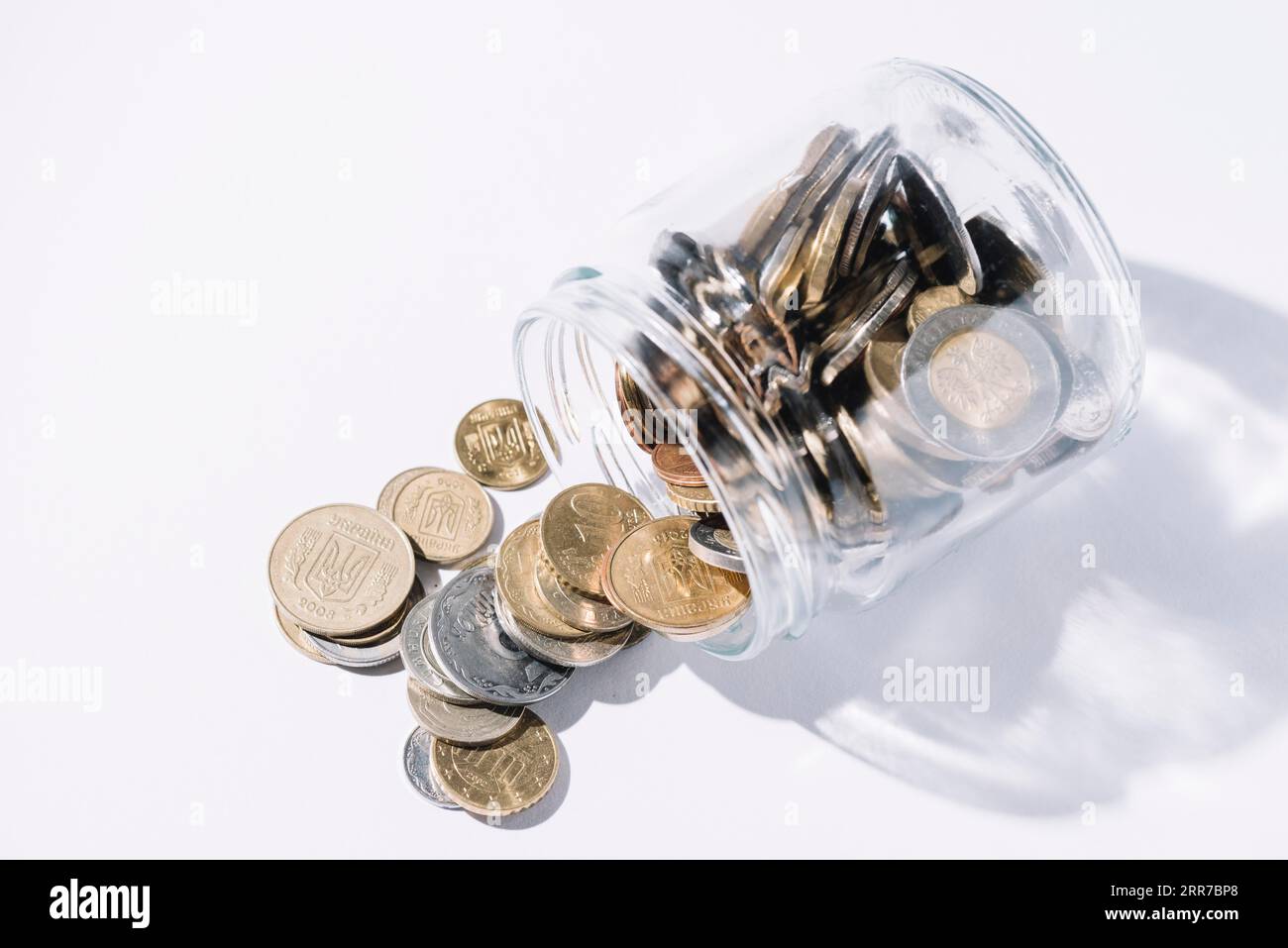 Fuoriuscite di monete da fondo bianco del contenitore di vetro Foto Stock