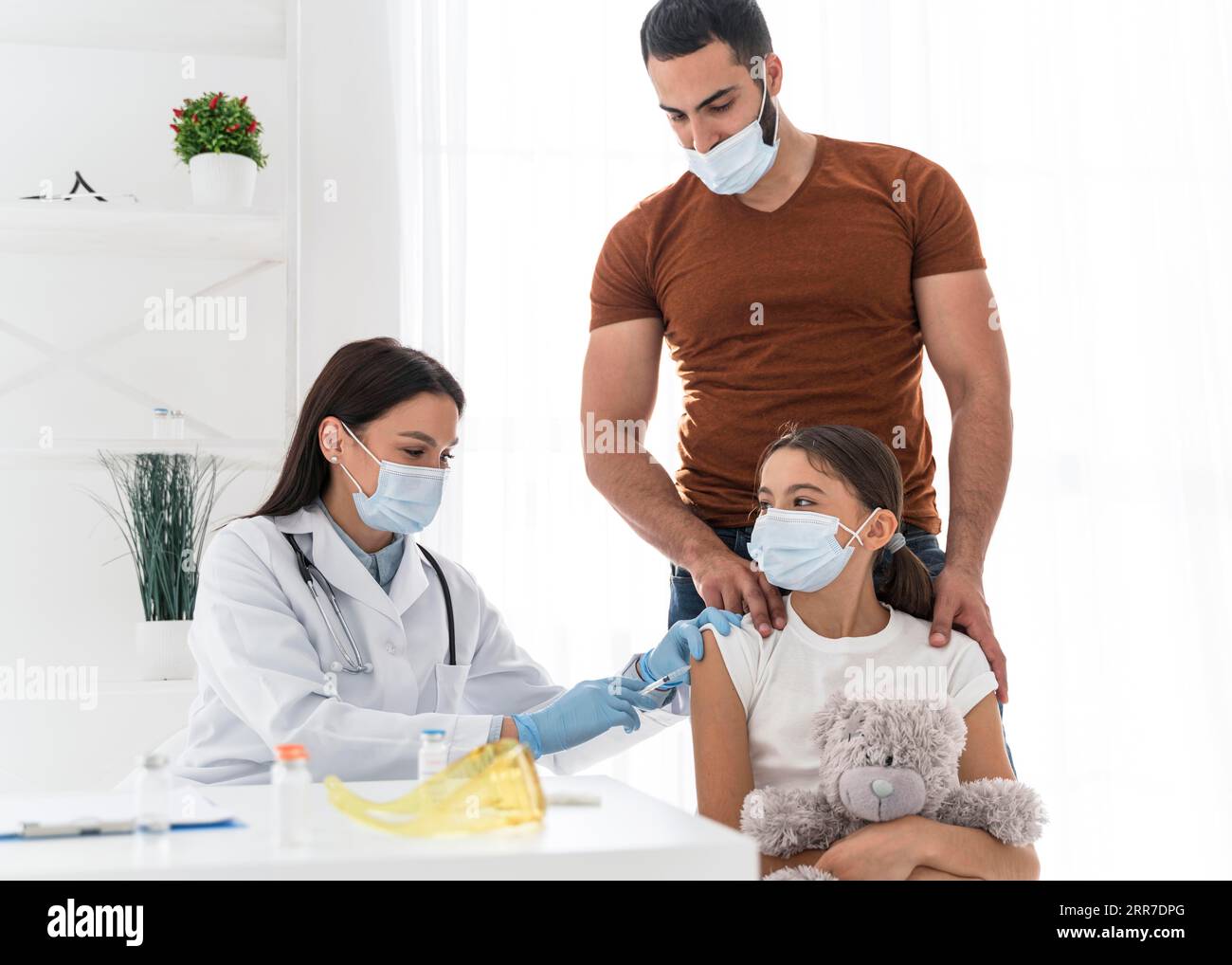 Ragazza che tiene il suo giocattolo mentre viene vaccinata Foto Stock