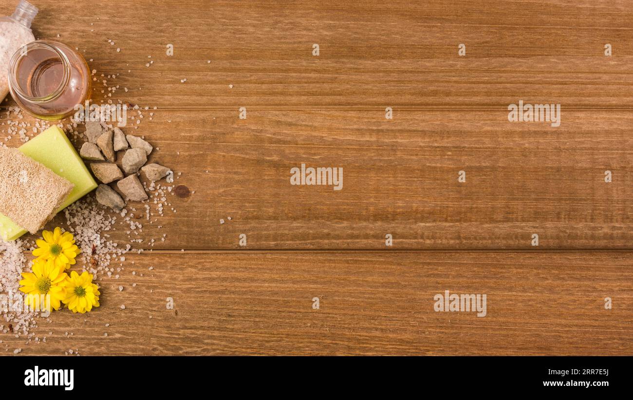 Vista panoramica fiori gialli pietre saline spugna loofah bottiglia di miele fondo in legno ruvido Foto Stock