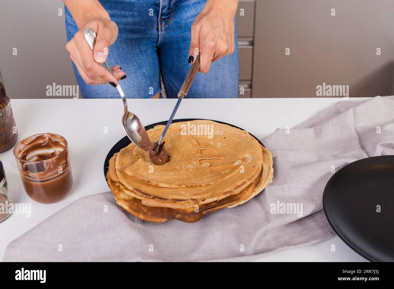 Primo piano della donna che spalma pancake al burro di arachidi con un coltello a cucchiaio Foto Stock