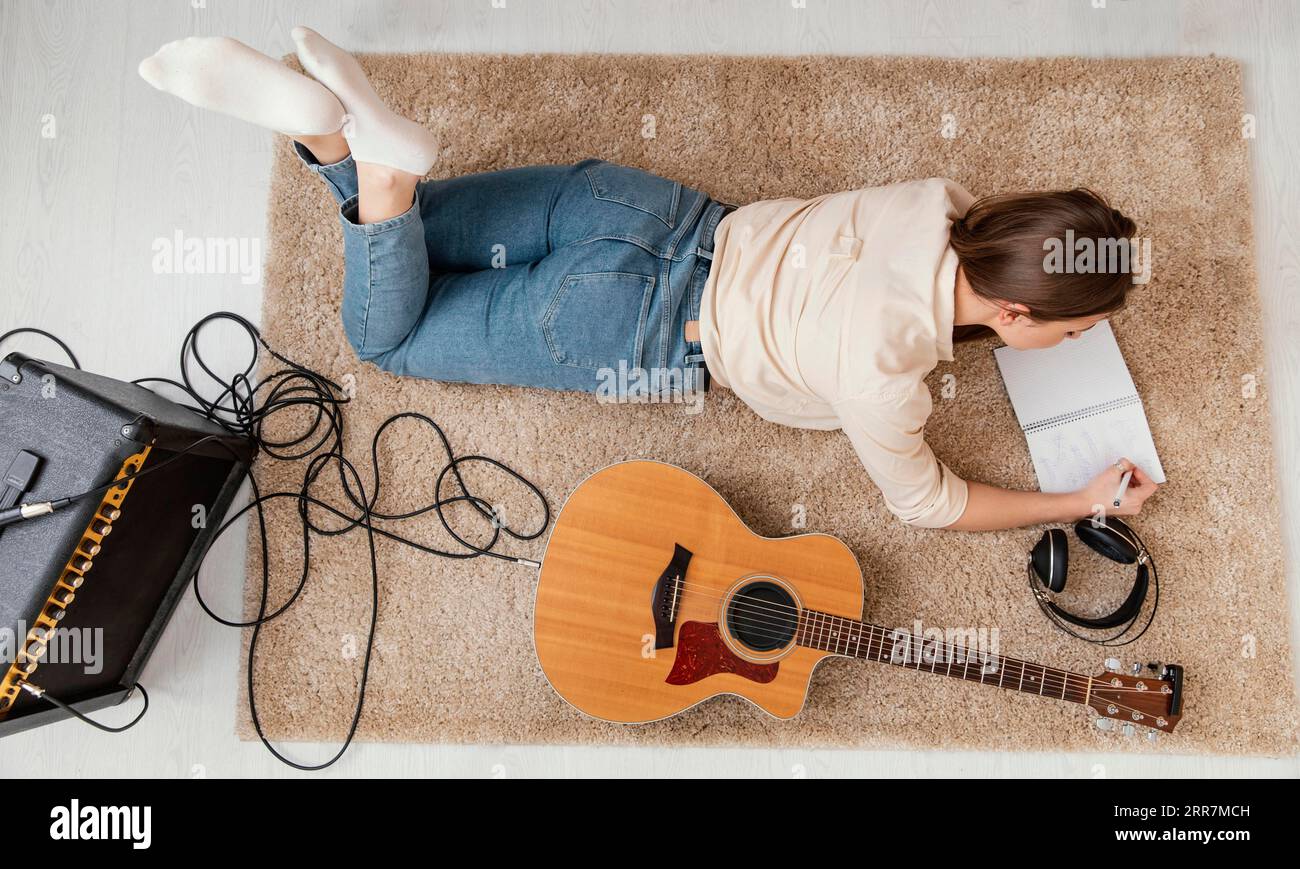 Cantautrice donna Flat Lay che scrive in casa canzoni con chitarra acustica in cuffia Foto Stock