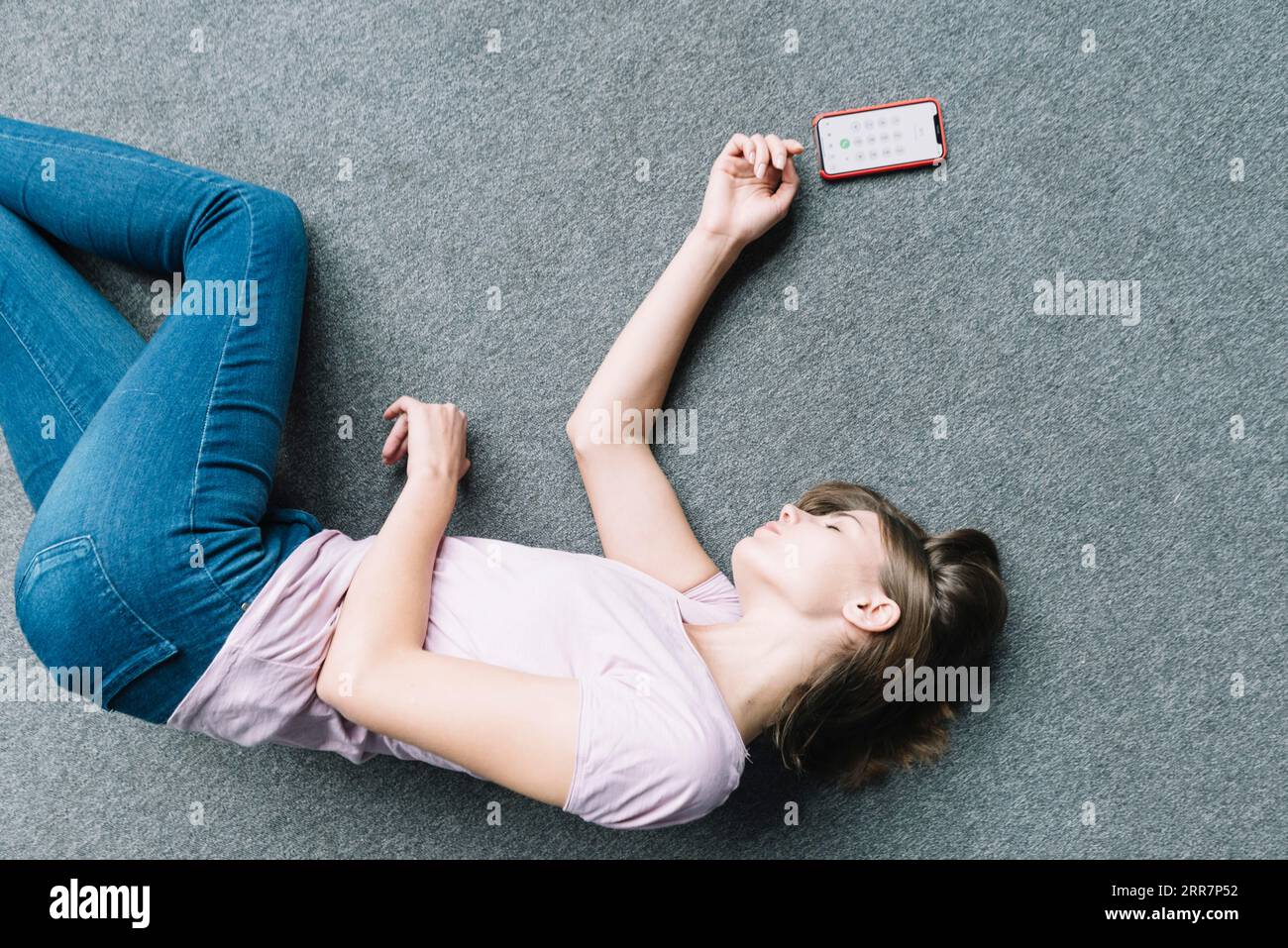 Giovane donna che giace inconsciamente tappeto vicino allo smartphone Foto Stock