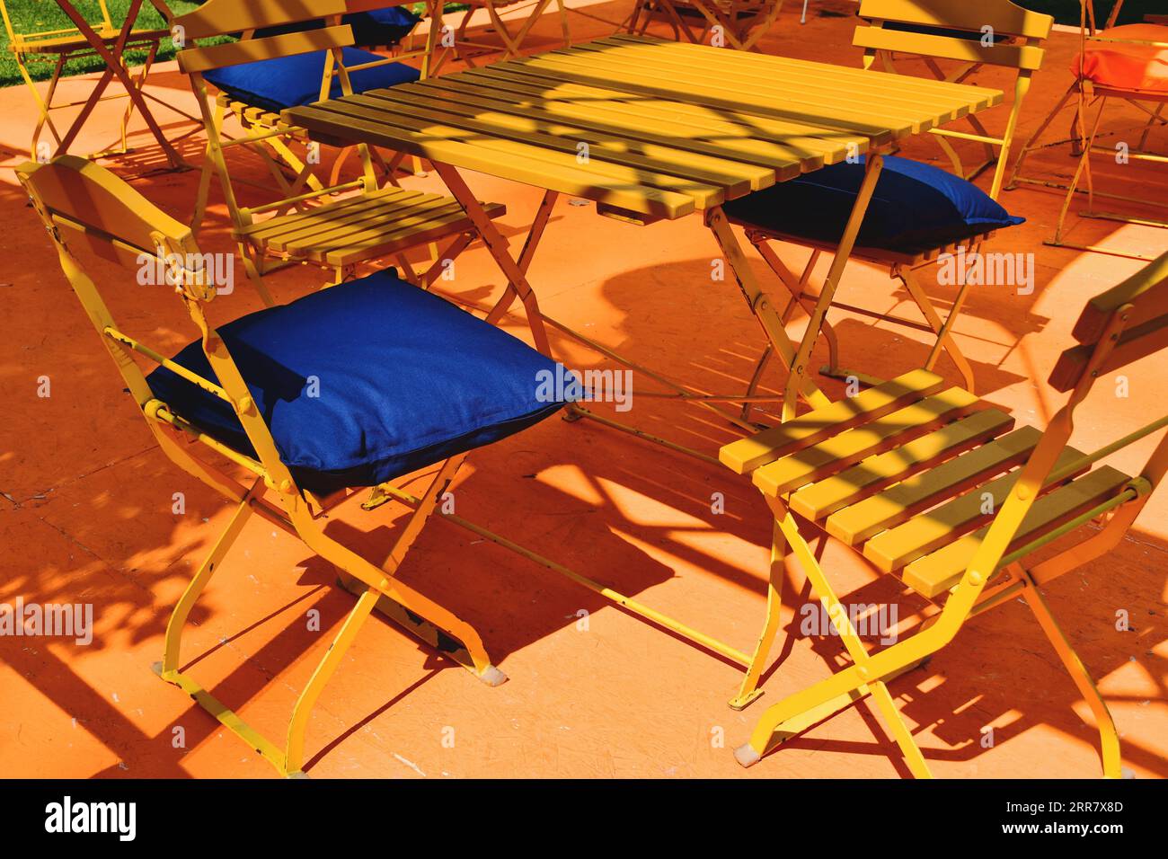 terrazza in legno di forma quadrata gialla e tavolo del ristorante. patio e terrazza. cuscino blu. forte contrasto. sedia pieghevole in legno e metallo. street cafe Foto Stock