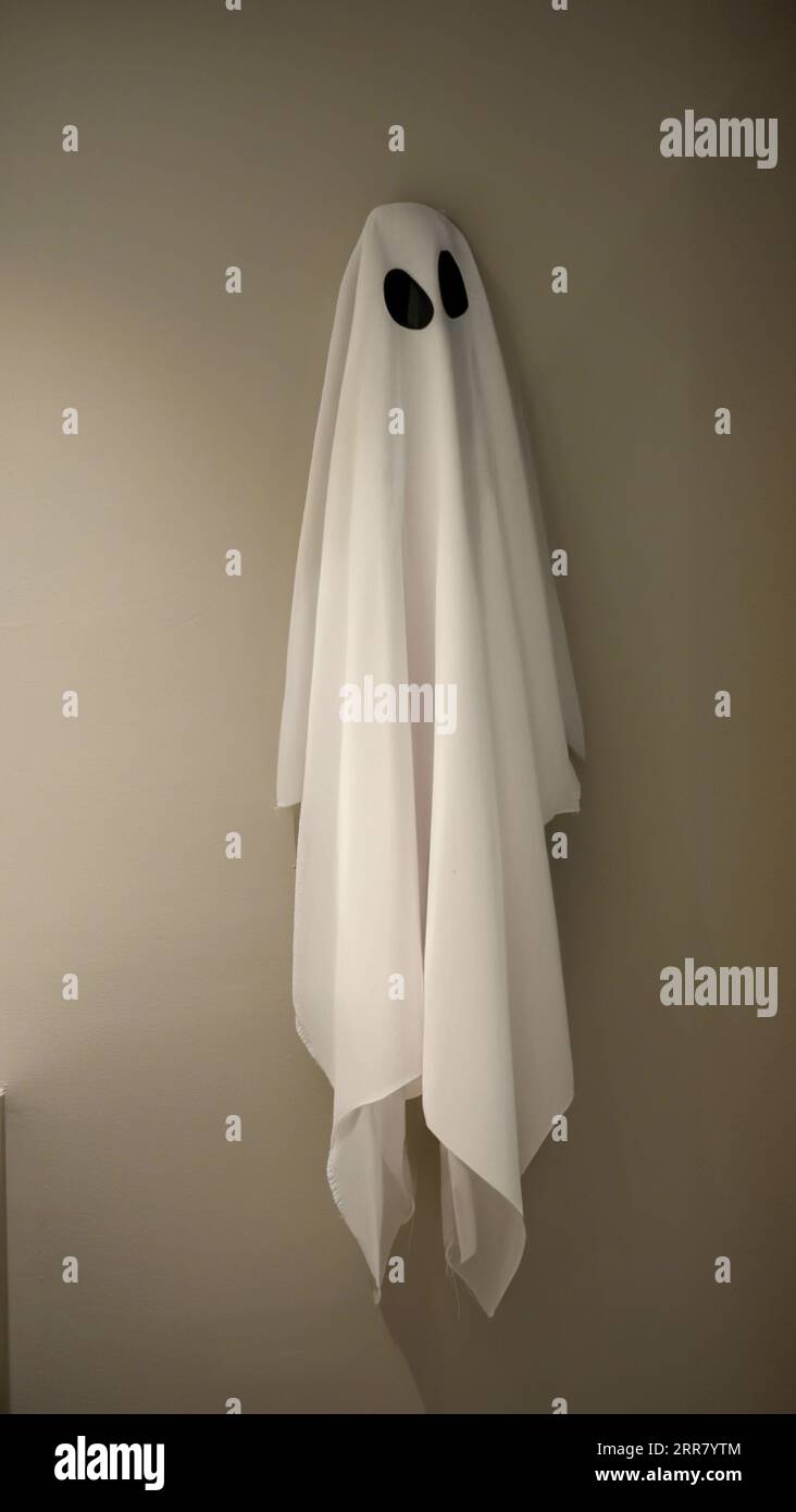 Un vestito bianco coperto da fantasmi è stato appeso al gancio al muro, rompere il tempo, fare una pausa, divertente concetto di Halloween, costume da festa, h Foto Stock