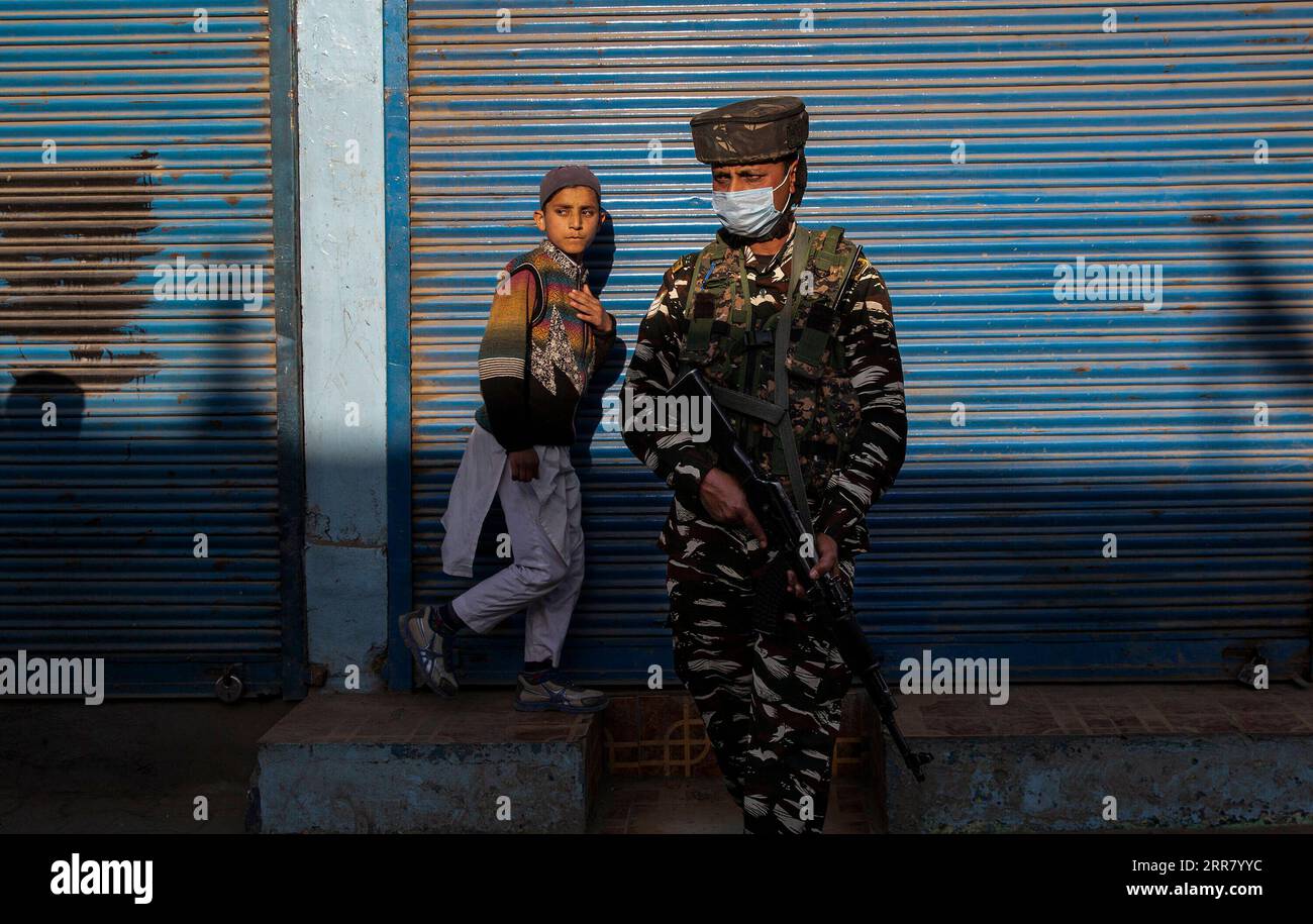 210409 -- SRINAGAR, 9 aprile 2021 -- un ragazzo cammina davanti a un gruppo di soldati paramilitari indiani, in piedi di guardia nel sito di un attacco a un gruppo di soldati dell'esercito territoriale nella città di Bijbehara nel distretto di Anantnag, a circa 44 km a sud della città di Srinagar, la capitale estiva del Kashmir controllato dagli indiani, il 9 aprile 2021. Uomini armati non identificati venerdì hanno ucciso un soldato fuori servizio appartenente all'esercito territoriale nel Kashmir controllato dagli indiani, hanno detto i funzionari. KASHMIR-BIJBEHARA-TERRITORY ARMY TROOPER-KILLING JAVEDXDAR PUBLICATIONXNOTXINXCHN Foto Stock