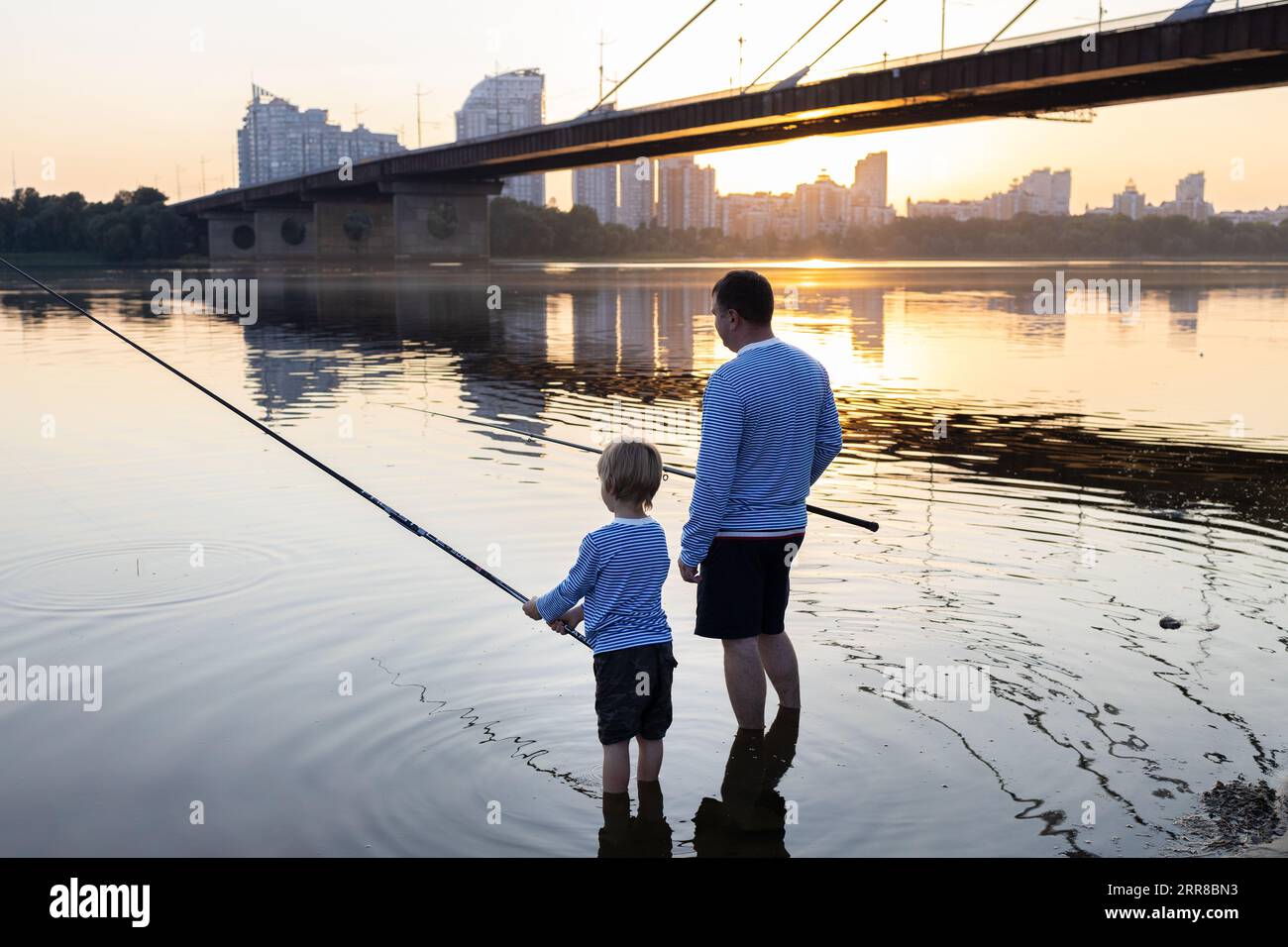 Padre e figlio stanno pescando insieme con canne da pesca nelle acque del fiume al tramonto. il concetto del giorno del padre. Passatempo divertente per tutta la famiglia Foto Stock