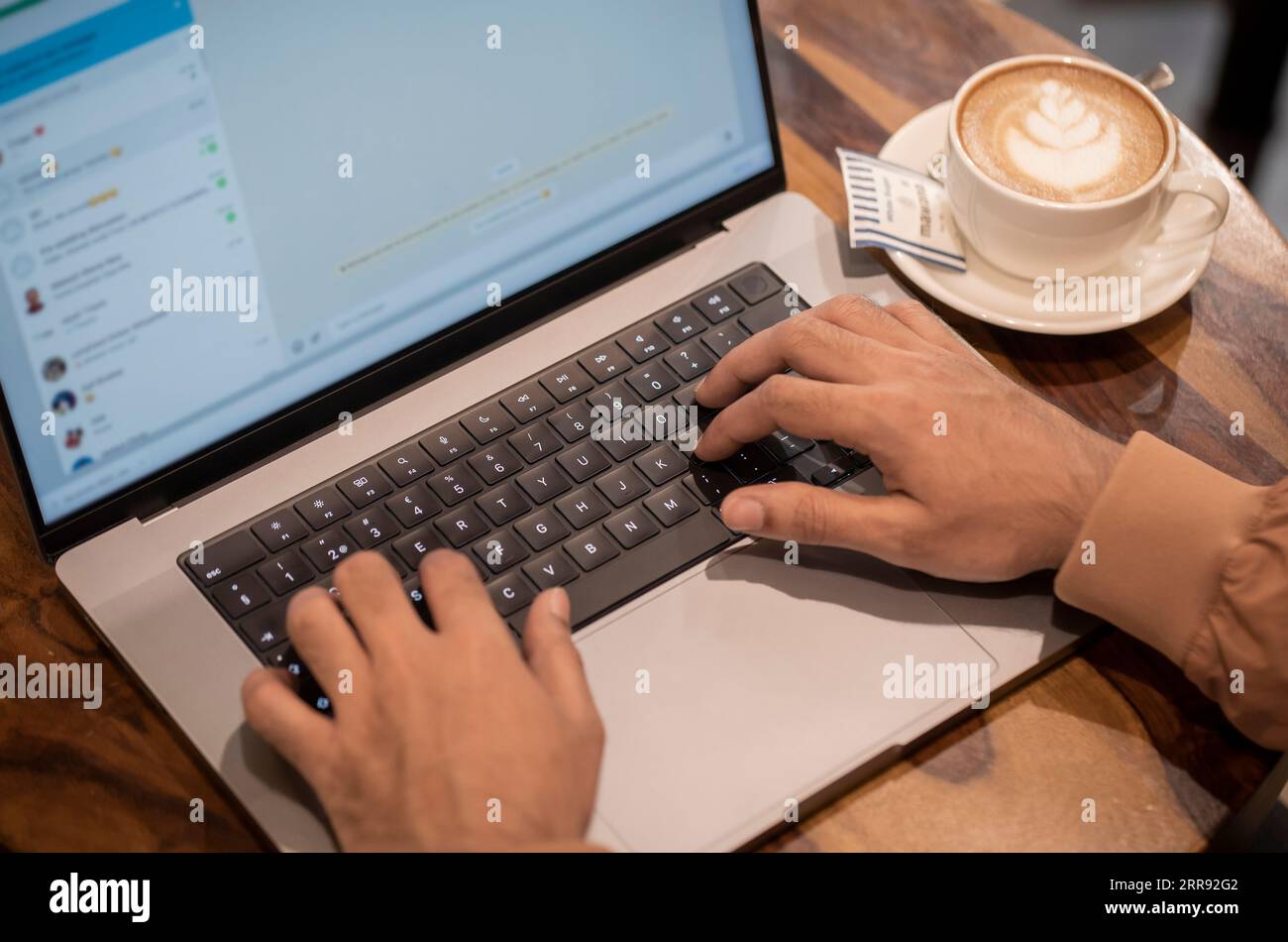 Mumbai, India 7 dicembre 2022 Un ragazzo sta scrivendo in una chiacchierata con un computer portatile, una tazza da caffè e un piattino tenuti da parte su un tavolo di legno Foto Stock