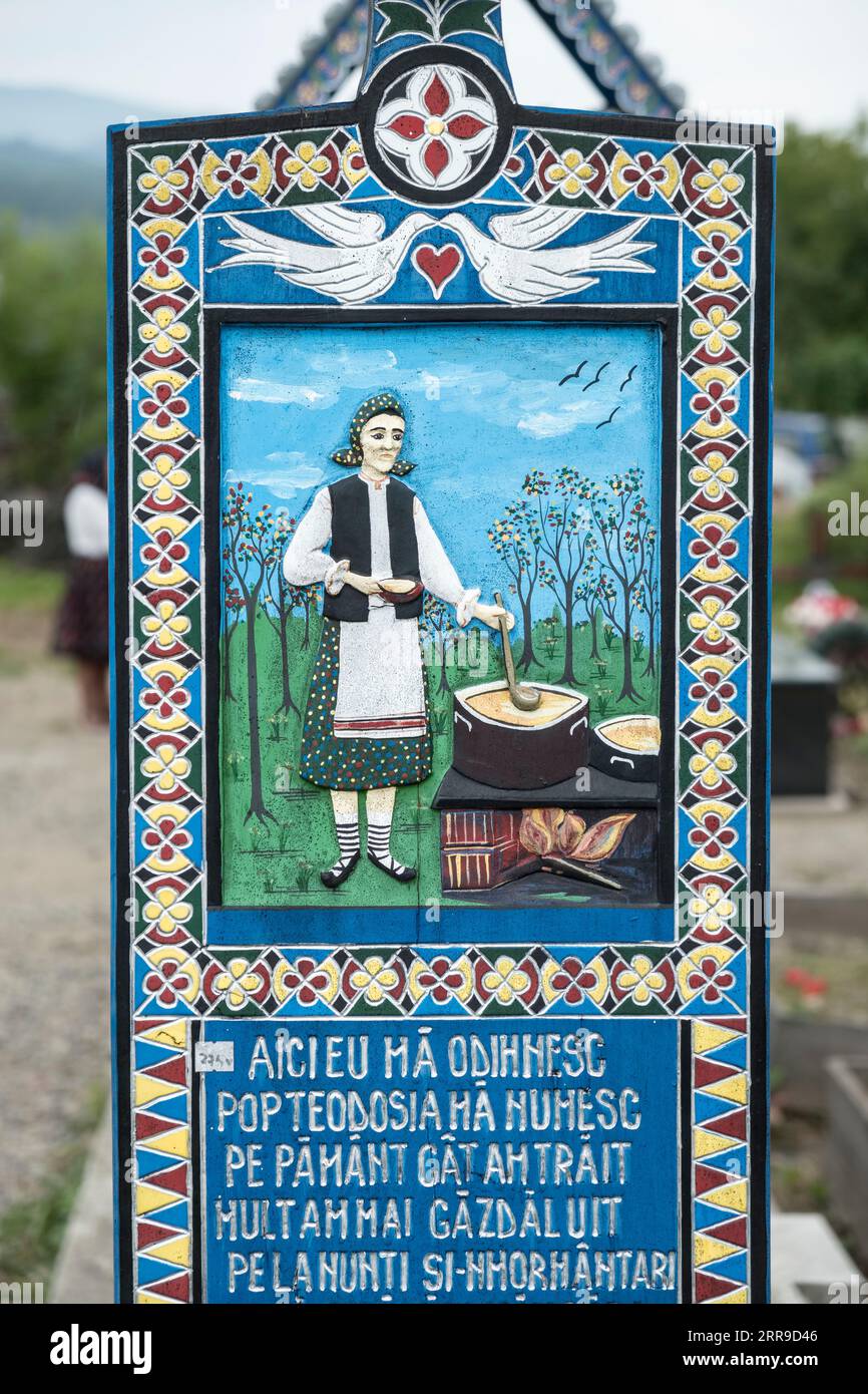 Una croce di legno scolpita dai colori vivaci segna la tomba di un cuoco nel famoso Cimitero Merry, nel villaggio di Săpânța, Maramureş, Romania Foto Stock