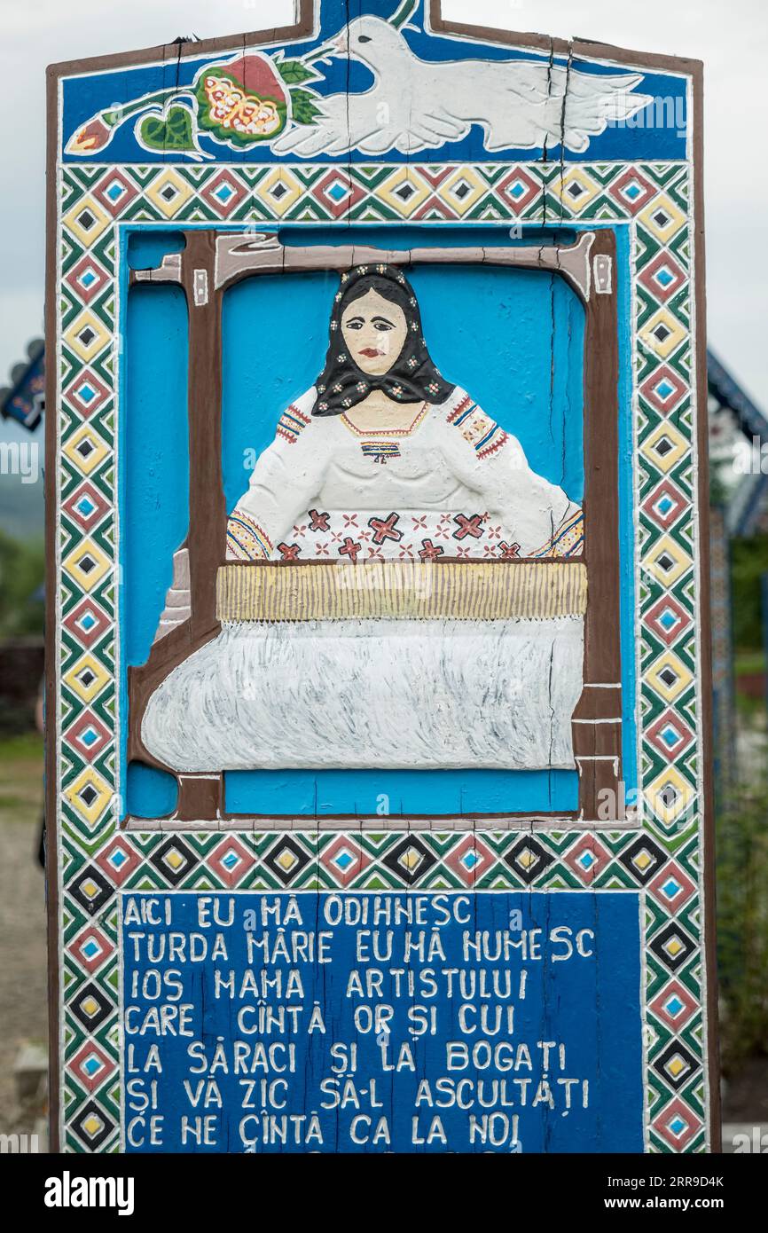Una croce di legno scolpita dai colori vivaci segna la tomba di un tessitore nel famoso cimitero allegro, nel villaggio di Săpânța, Maramureş, Romania Foto Stock
