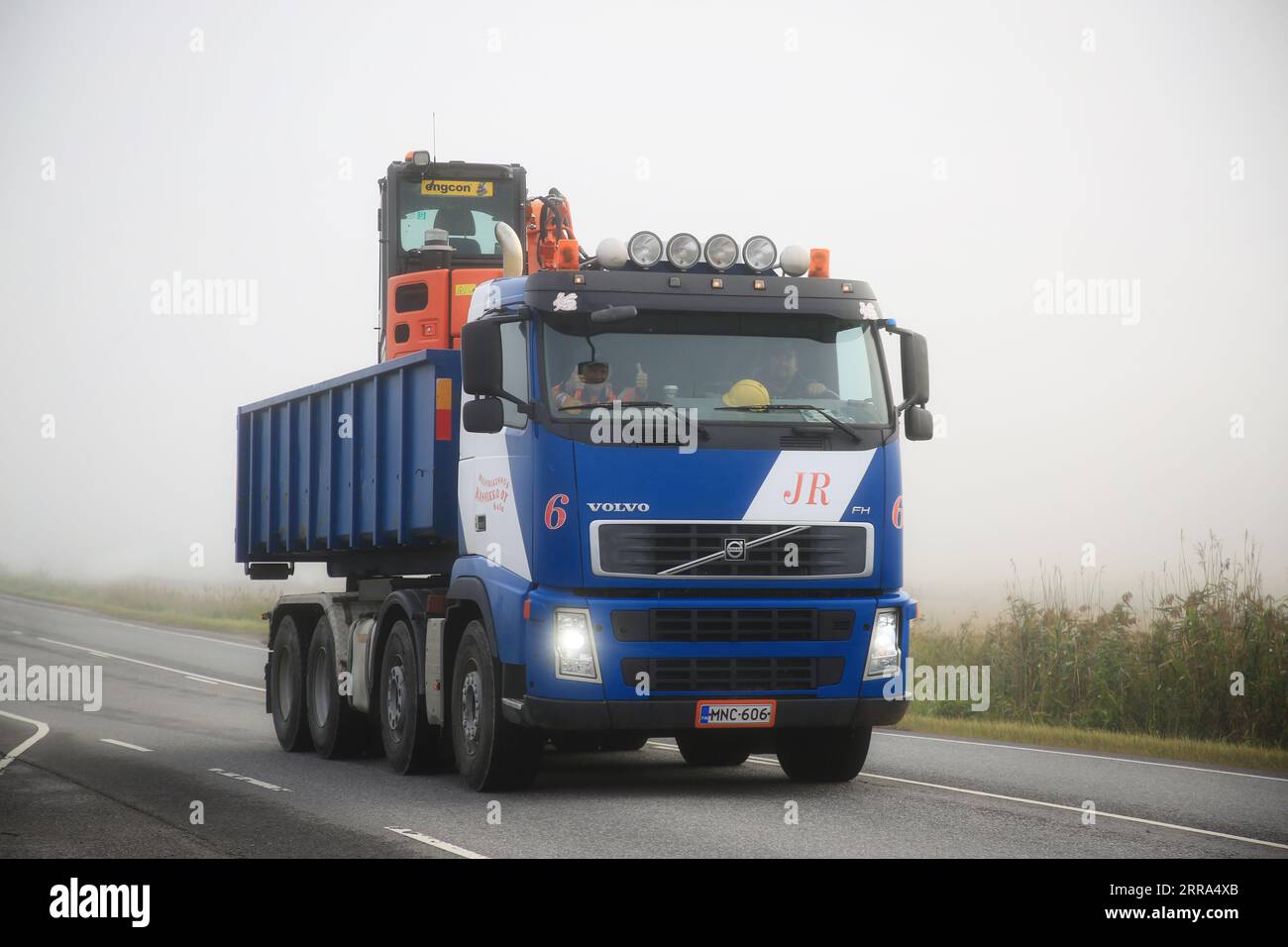 Il camion ribaltabile Volvo bianco-blu di Maanrakennus Rannikko Oy trasporta i macchinari Engcon in una mattinata nebbiosa. Salo, Finlandia. 25 agosto 2023. Foto Stock