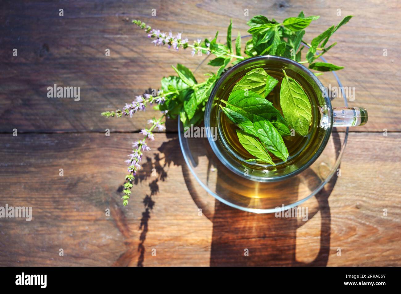 Tè alle erbe da foglie di menta piperita fresca e fiori in una tazza di vetro su un tavolo rustico in legno, vista dall'alto, spazio copia, fuoco selezionato, n Foto Stock