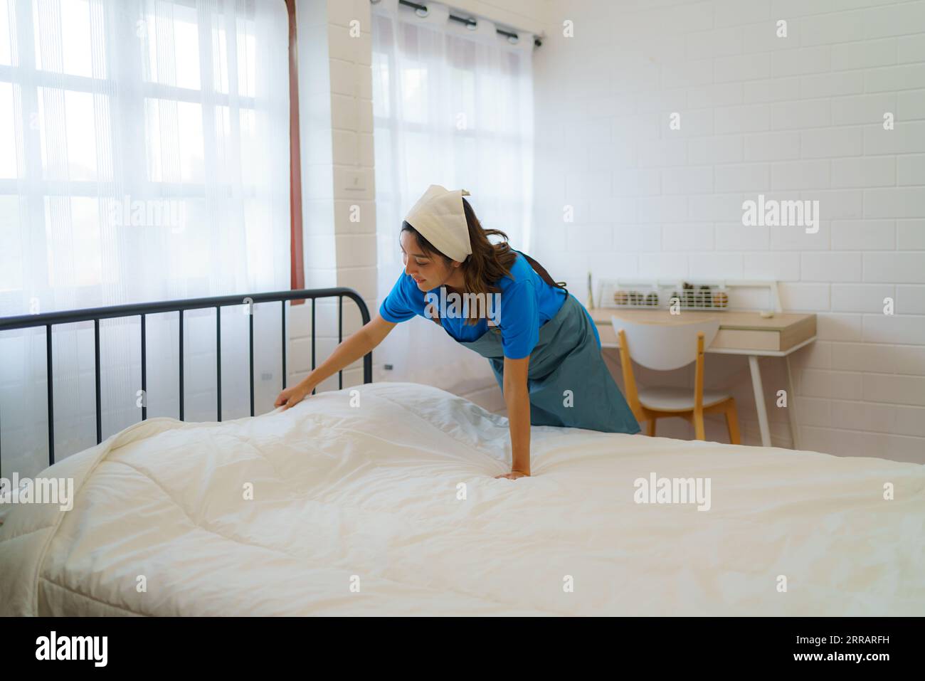 Nella tranquilla camera da letto, una casalinga asiatica organizza meticolosamente le coperte, infondendo calore e ordine, trasformando un letto in un'intima oasi di comfort. Foto Stock