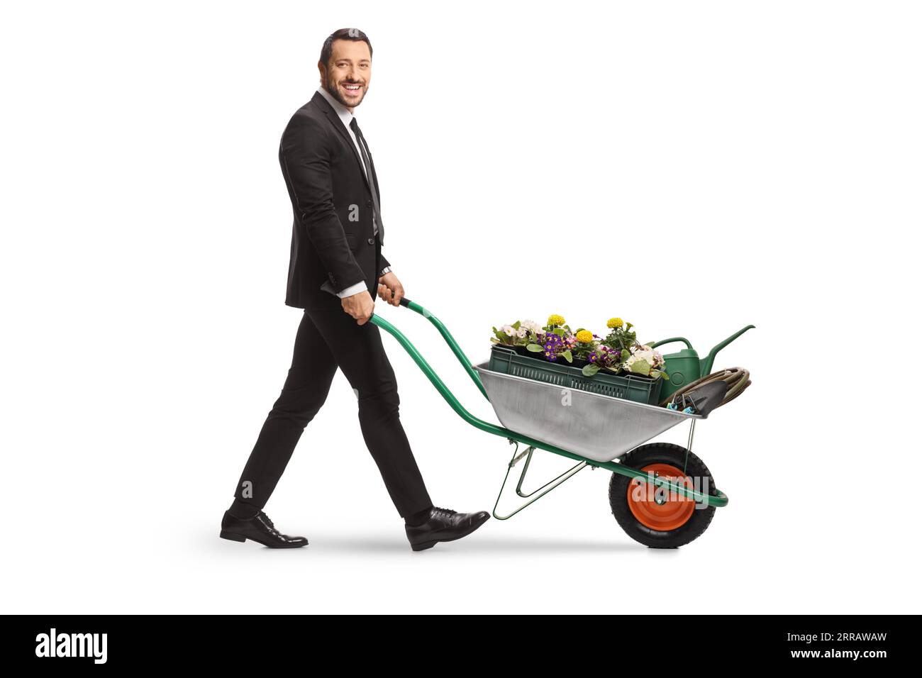 Foto a profilo completo di un uomo d'affari che spinge una carriola con fiori e innaffiatura può essere isolato su sfondo bianco Foto Stock