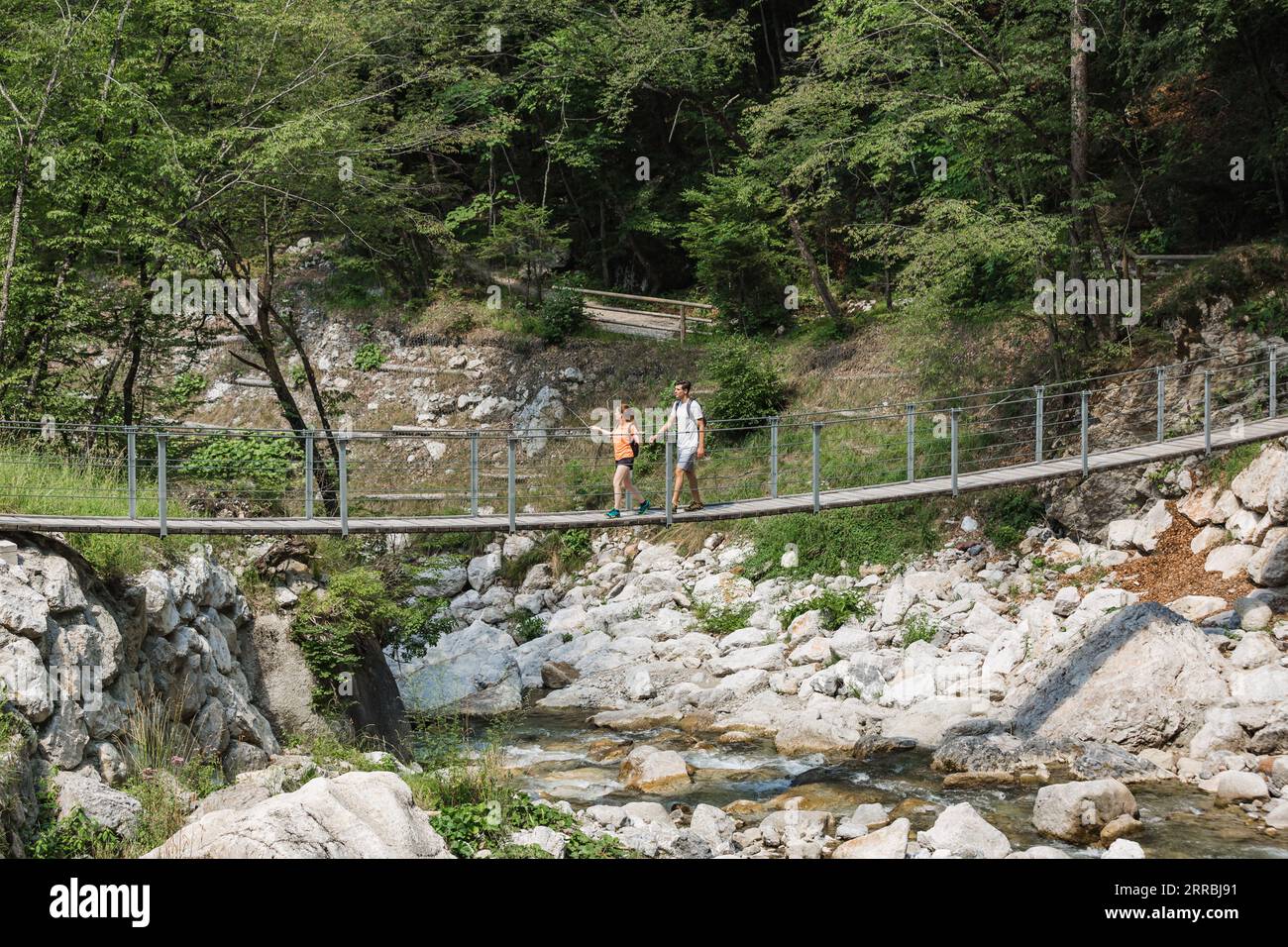 Giovani escursionisti attivi, uomo e donna che camminano su un torrente di montagna che scorre tra grandi e belle rocce. Concetto di esplorazione della natura. Foto Stock