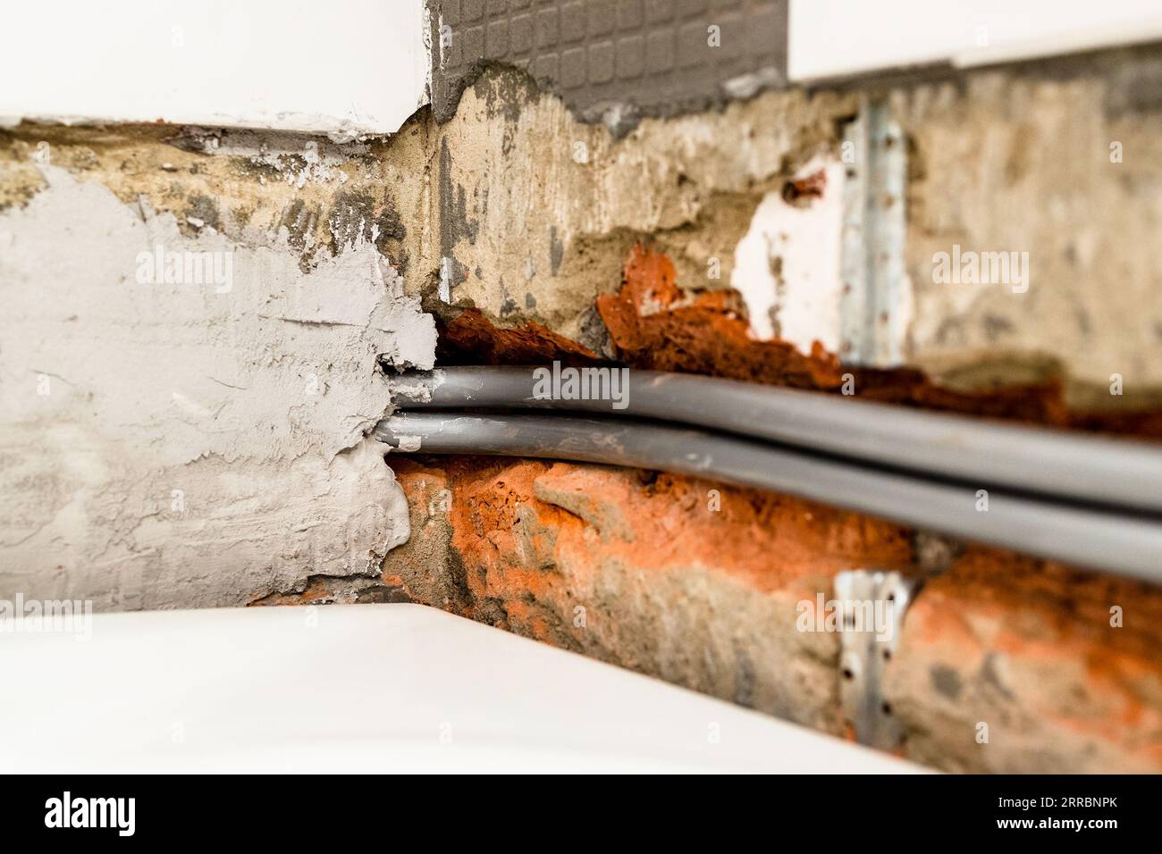 installazione di nuovi tubi idraulici flessibili in polietilene su pareti in mattoni scalpellati sopra la vasca da bagno bianca sotto le piastrelle in ceramica rimosse durante l'installazione di Foto Stock