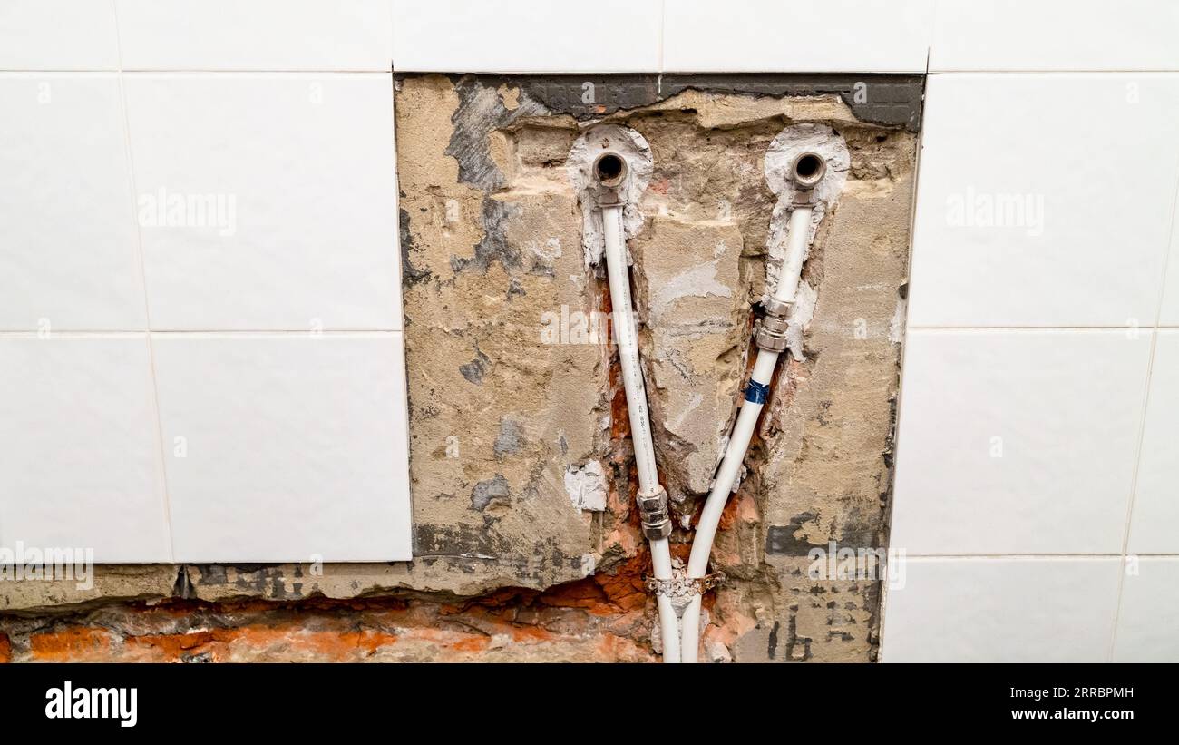 vecchia fornitura di acqua per rubinetto in bagno e tubazioni con tubi in metallo-plastica in mattoni scalpellati sotto le piastrelle di ceramica rimosse Foto Stock
