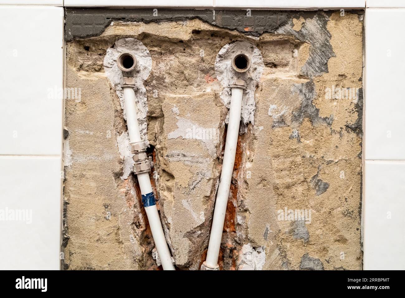 vecchio impianto idraulico con tubi in metallo-plastica in mattoni scalpellati sotto le piastrelle in ceramica rimosse Foto Stock