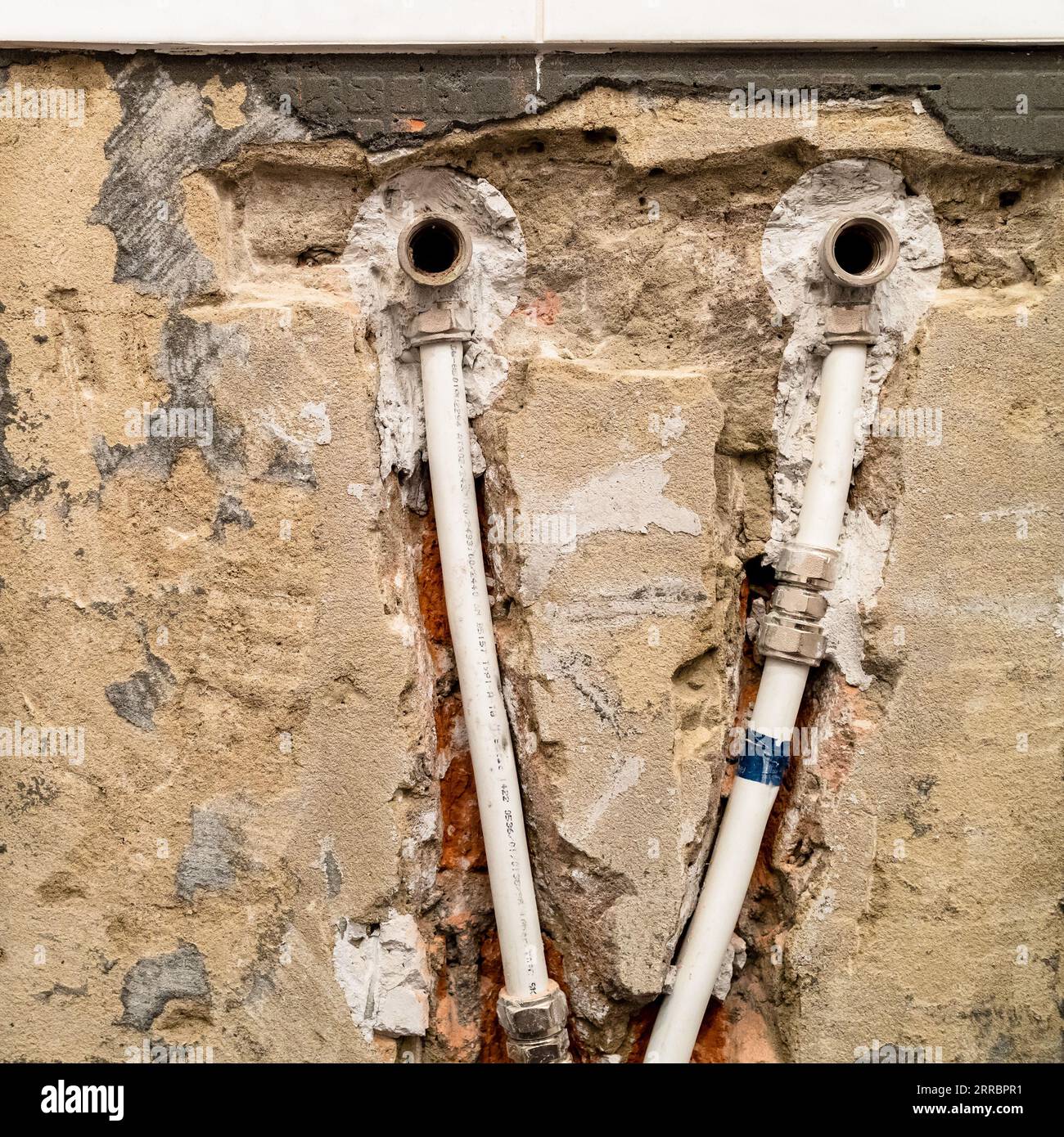 vecchia alimentazione idrica con primo piano dei tubi in metallo-plastica in parete cesellata Foto Stock