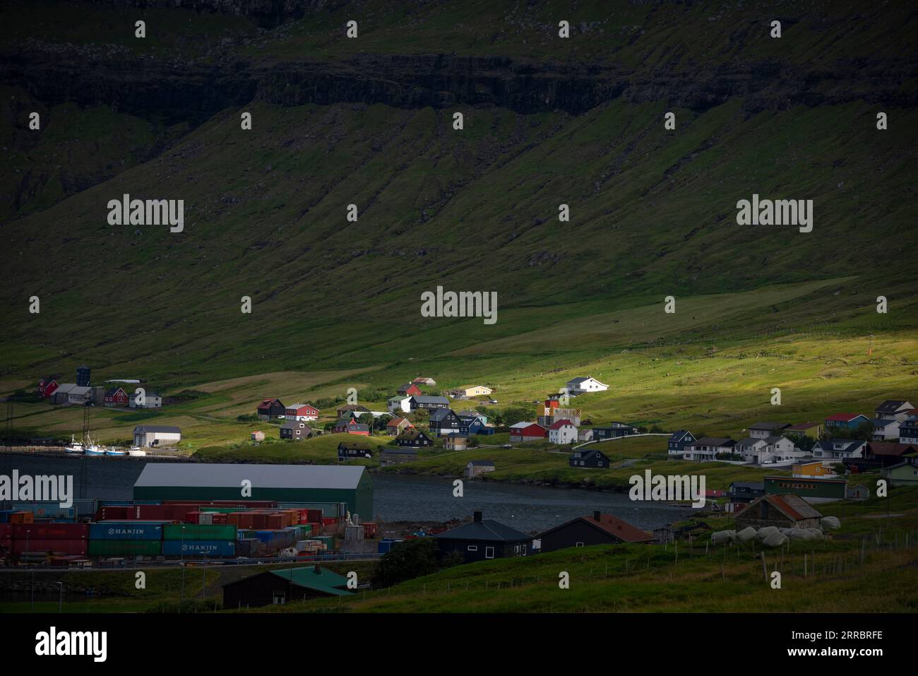 La luce mattutina attraversa la fitta copertura nuvolosa per attraversare il villaggio di Kollafjør∂sull'isola Streymoy nelle Isole Faroe. Foto Stock