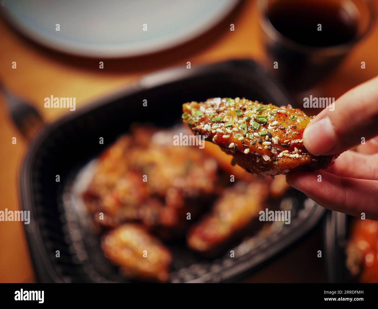 Un uomo che raccoglie un'ala di pollo in stile coreano. Cibo di strada asiatico. Concetto di consegna Foto Stock