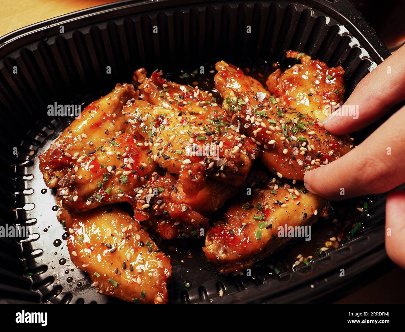 La mano di un uomo che raccoglie le ali di pollo coreane con salsa. 치킨. Cibo di strada asiatico. Concetto di consegna Foto Stock