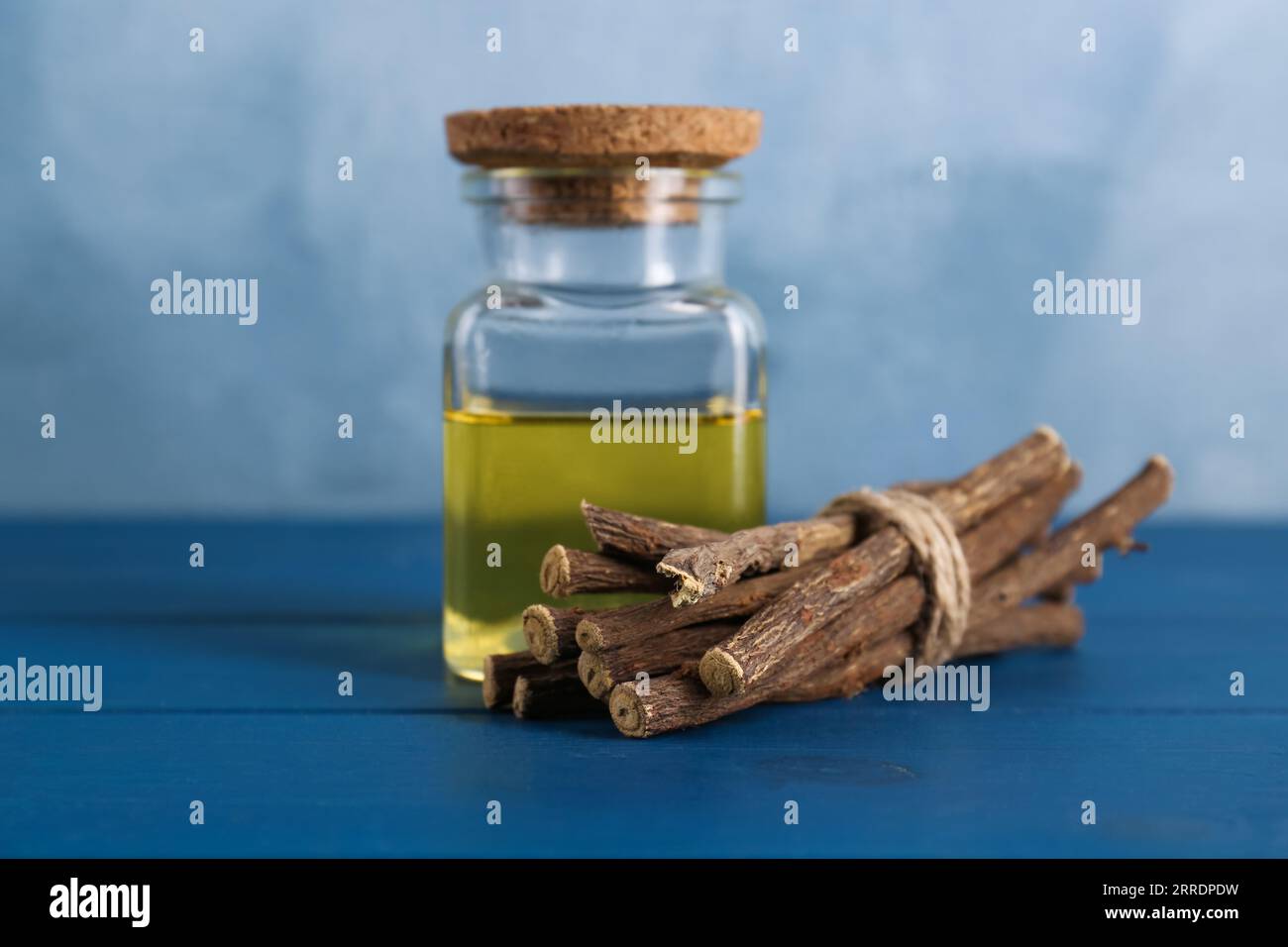 Bastoncini secchi di radice di liquirizia e olio essenziale su tavola di legno blu Foto Stock