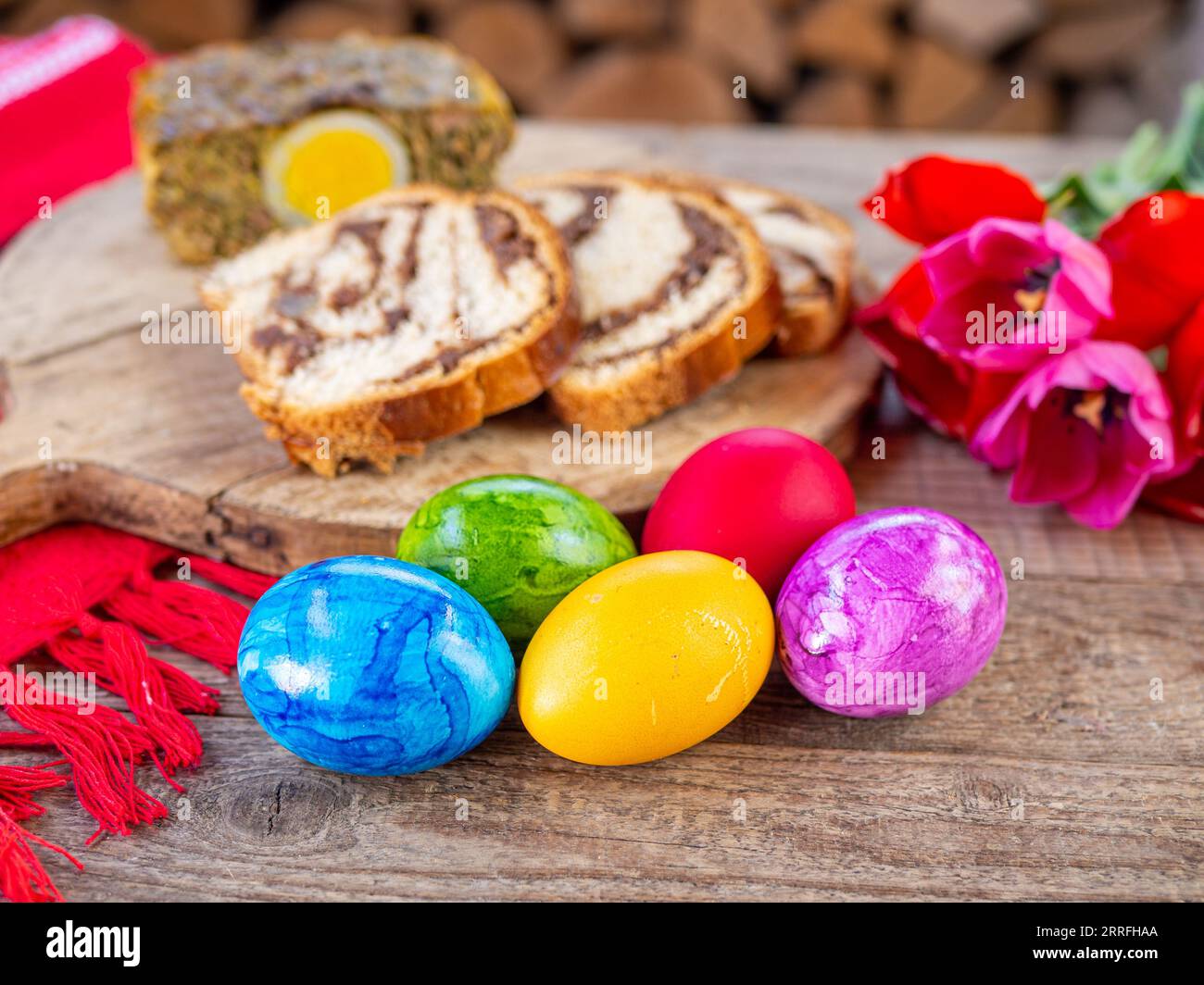Tradizionale piatto pasquale rumeno, cozonac o pane dolce su tavola di legno, uova di pasqua colorate e fiori bianchi di narciso Foto Stock